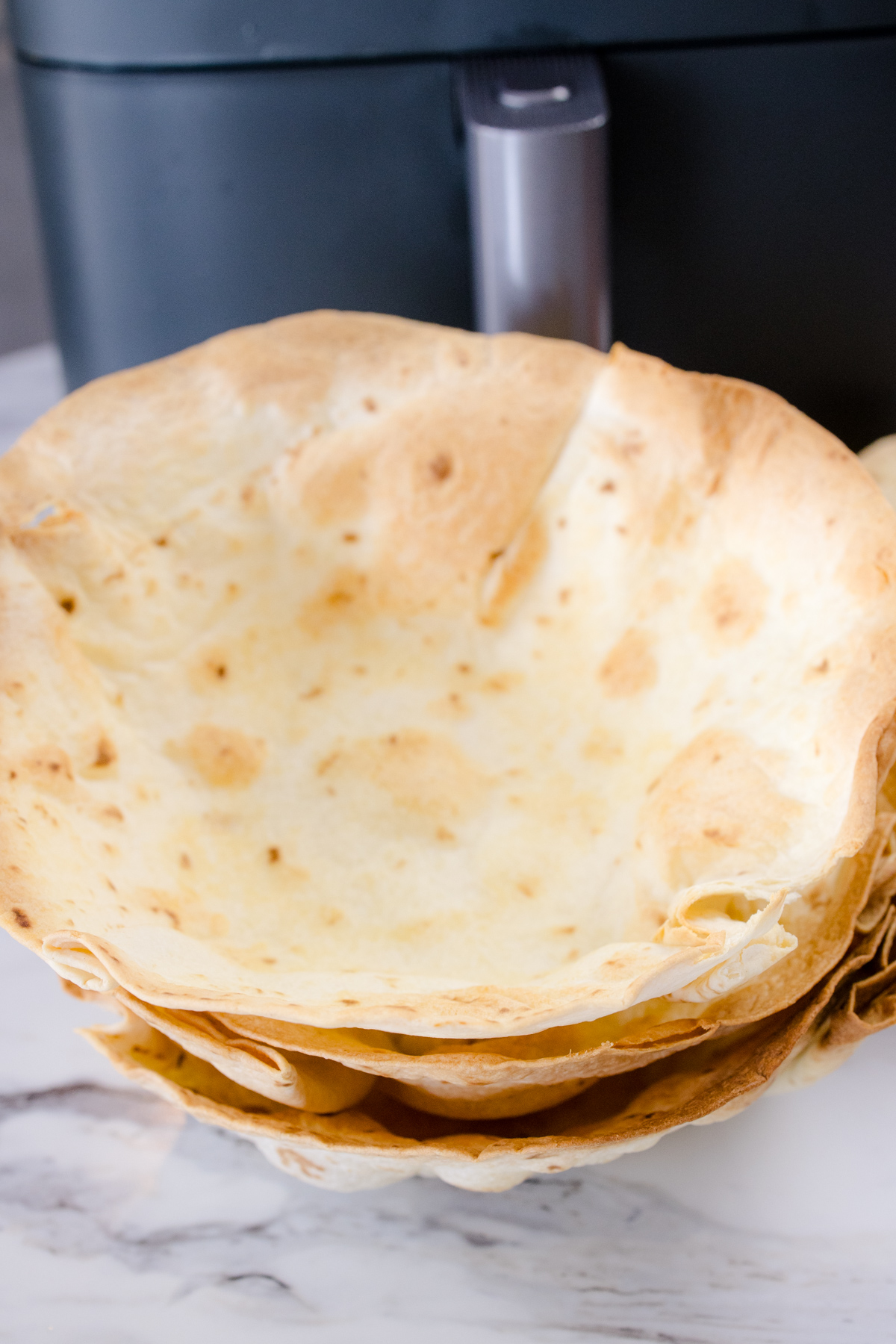 A stack of cooked Air Fryer Flour Tortilla Bowls in front of an air fryer.