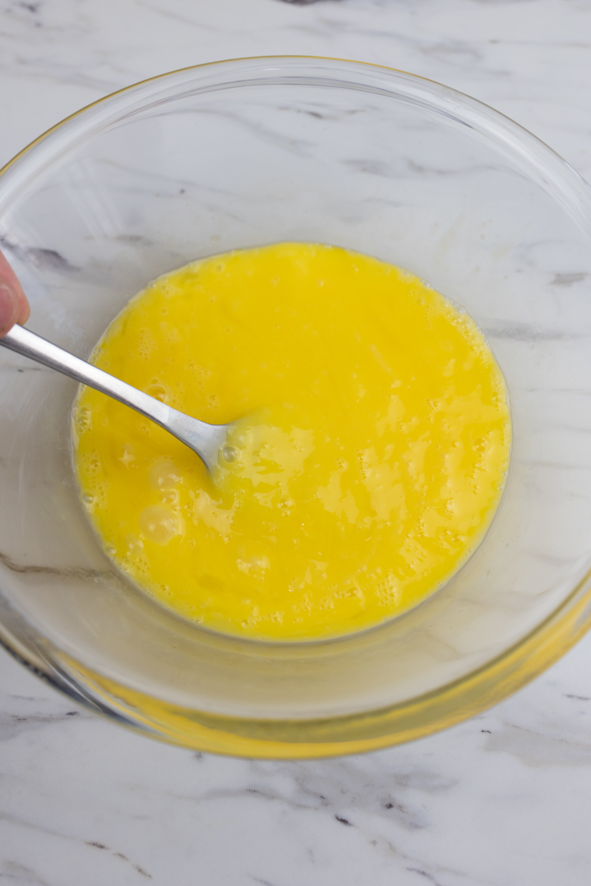 A fork whisking the egg mixture for Air Fryer French Toast in a large glass mixing bowl.