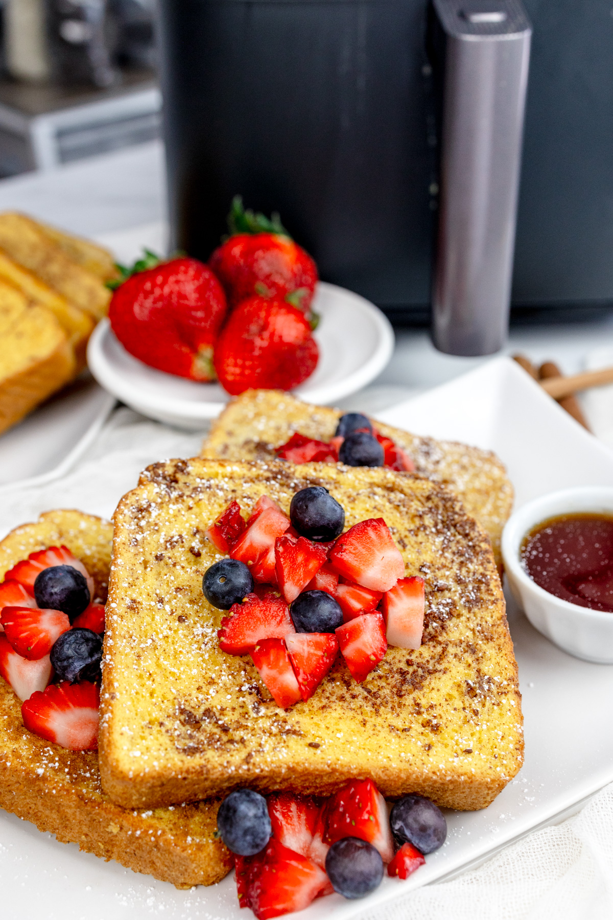 Air Fryer French Toast with syrup and berries on top on a rectangular white plate and more berries.