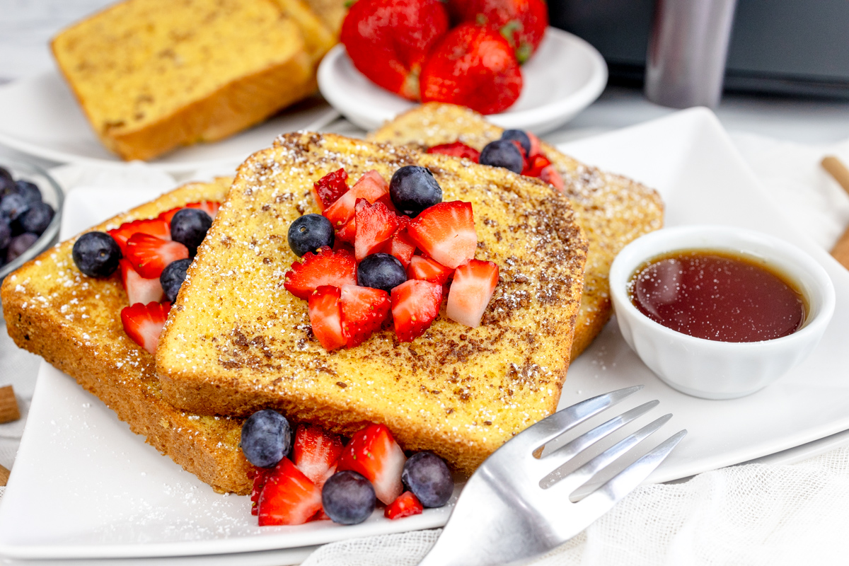 Air Fryer French Toast with syrup and berries on top on a rectangular white plate and more berries.