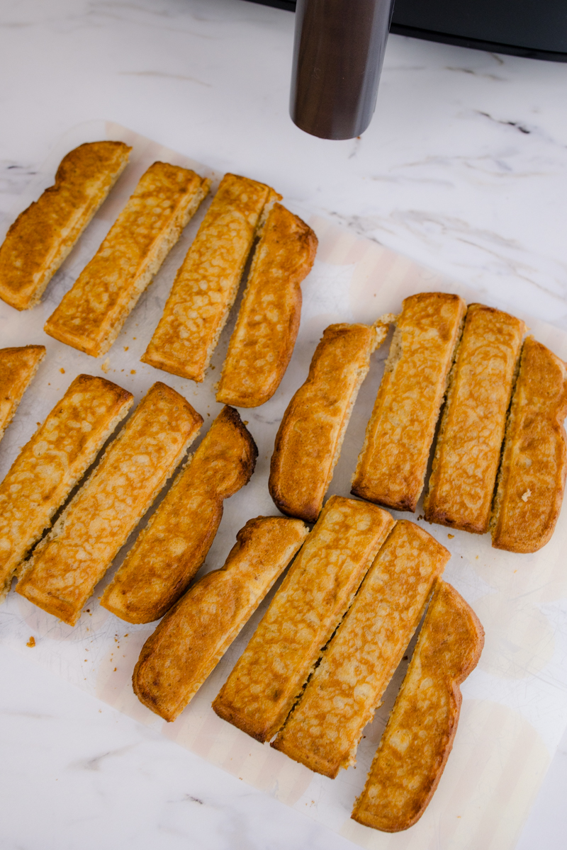 Cooked Air Fryer Frozen French Toast Sticks on a white surface.