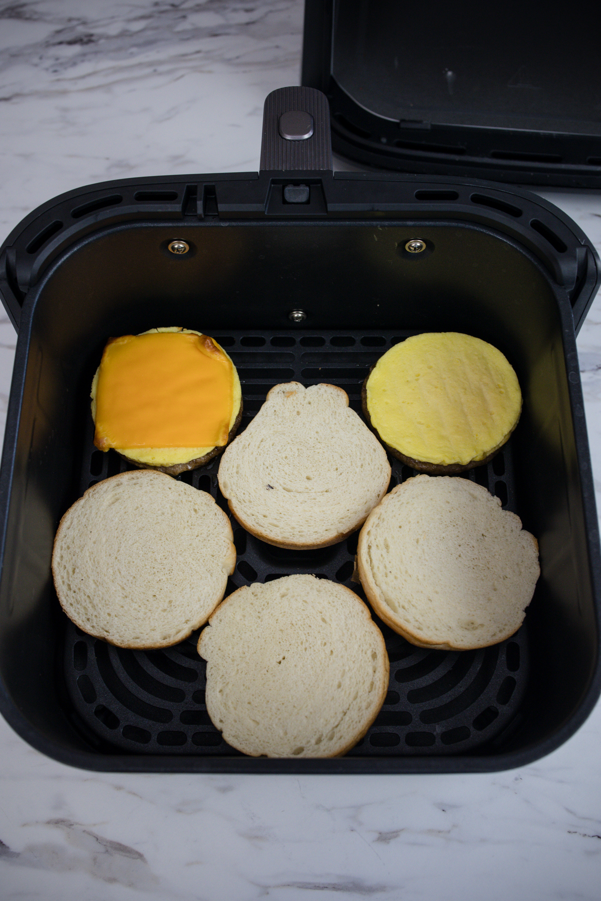 Two Jimmy Dean Breakfast Sandwiches in an air fryer, separated into their different parts.