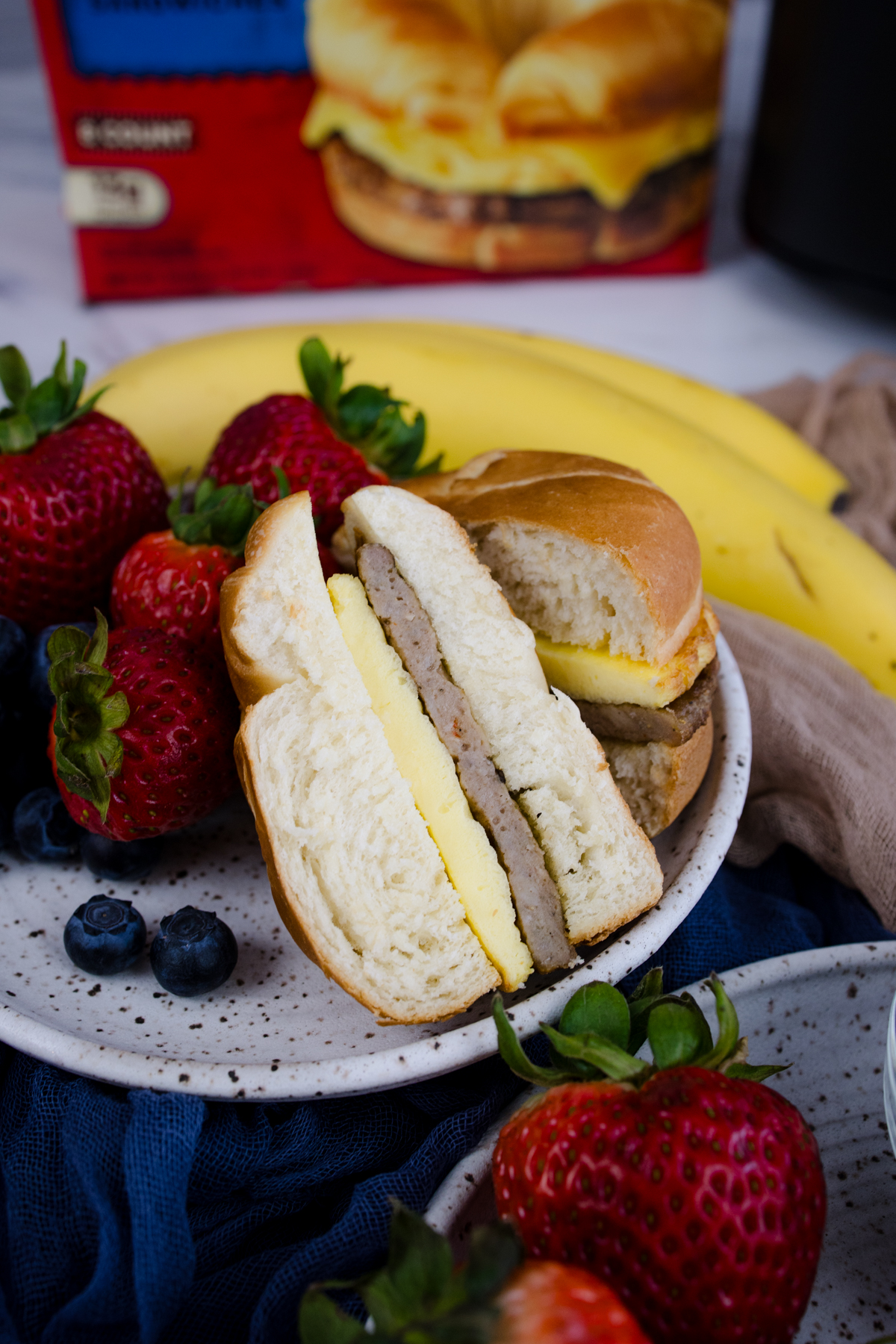 Jimmy Dean Breakfast Sandwich sliced in half on a plate with strawberries and blueberries.