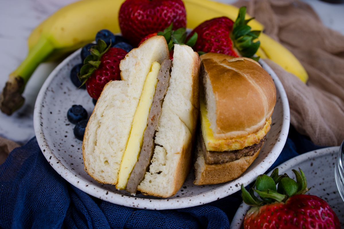 Jimmy Dean Breakfast Sandwich sliced in half on a plate with strawberries and blueberries.