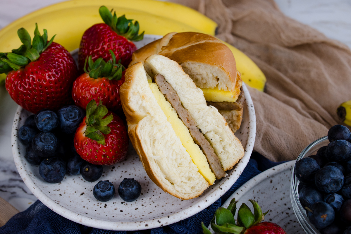 Jimmy Dean Breakfast Sandwich sliced in half on a plate with strawberries and blueberries.