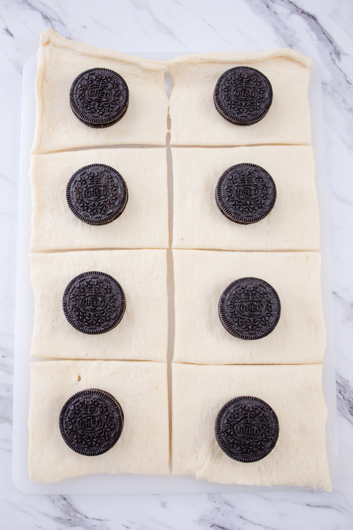 Crescent roll dough stretched in a rectangle on a white surface, sliced with a pizza cutter, with oreos placed into the squares of dough.