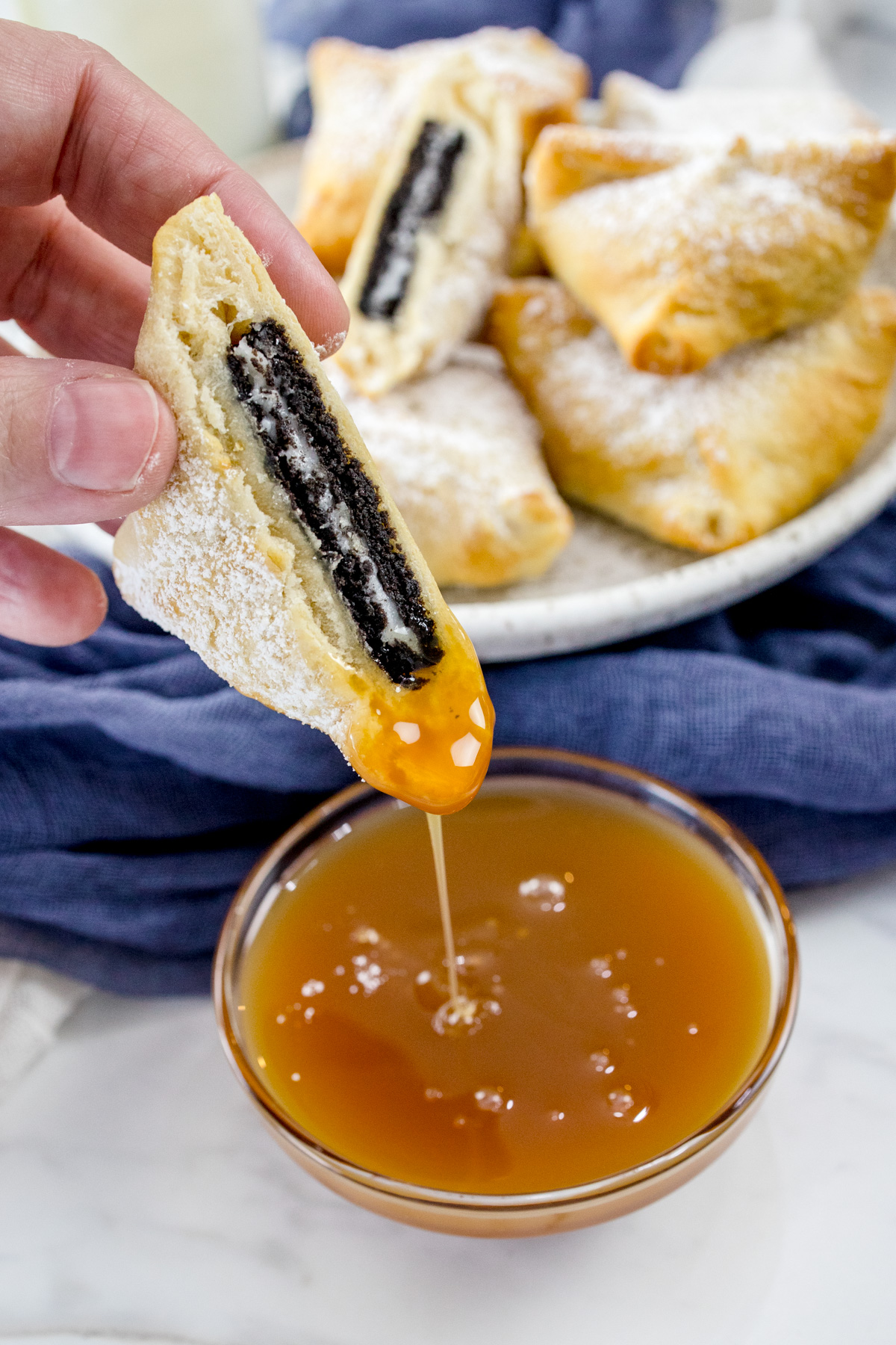 Half of a sliced Air Fryer Oreo being dipped in sauce with other Air Fryer Oreos in the background.