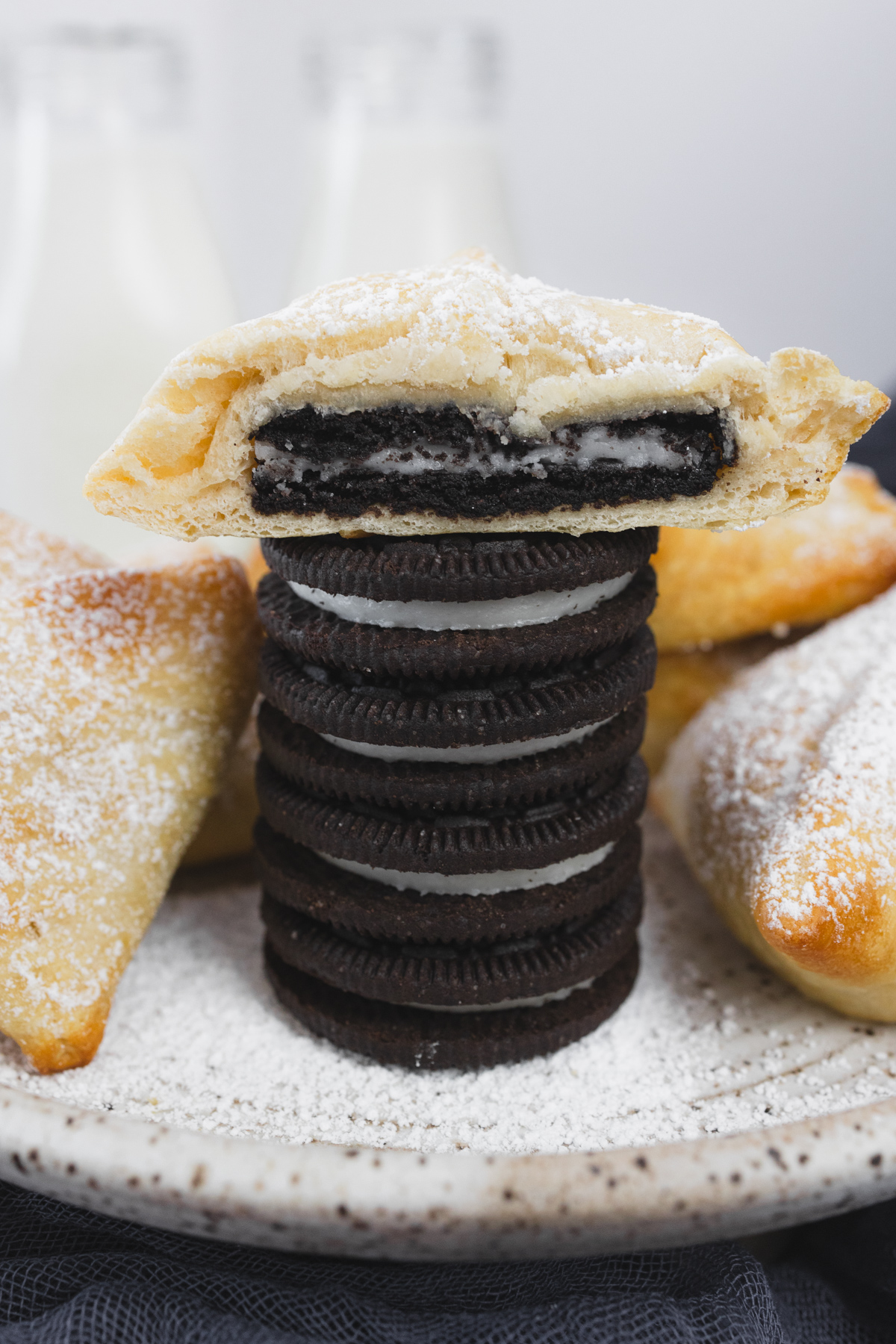 A stack of Oreos with half of an Air Fryer Fried Oreo on top of it, on a white plate with other fried oreos around it.