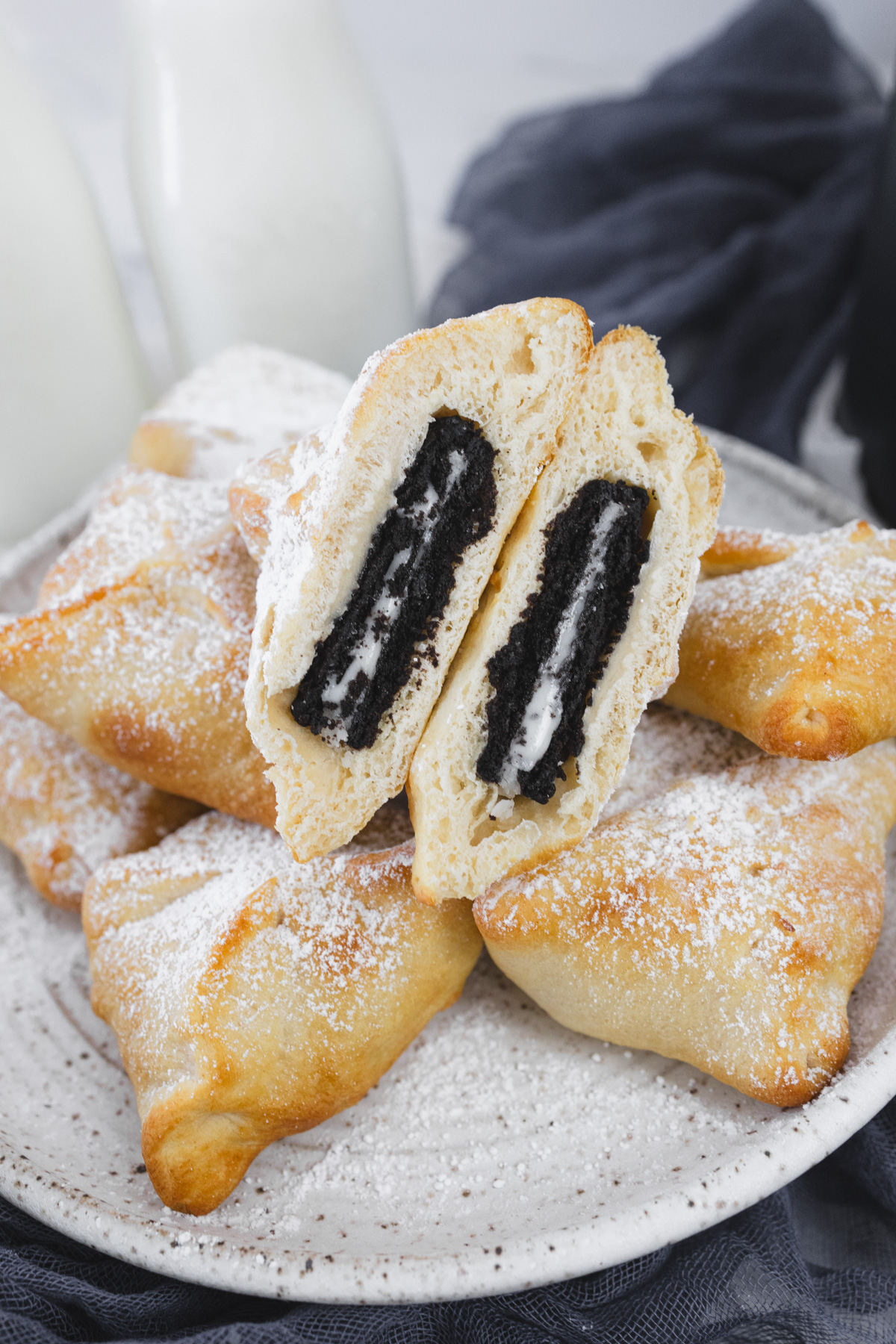 Air Fryer Fried Oreos on a white plate. The one in the foreground is sliced in half, exposing the middle.