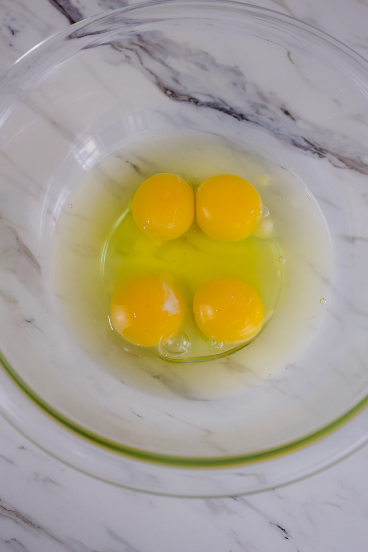 A top view of 4 egg yolks and whites in a glass mixing bowl.