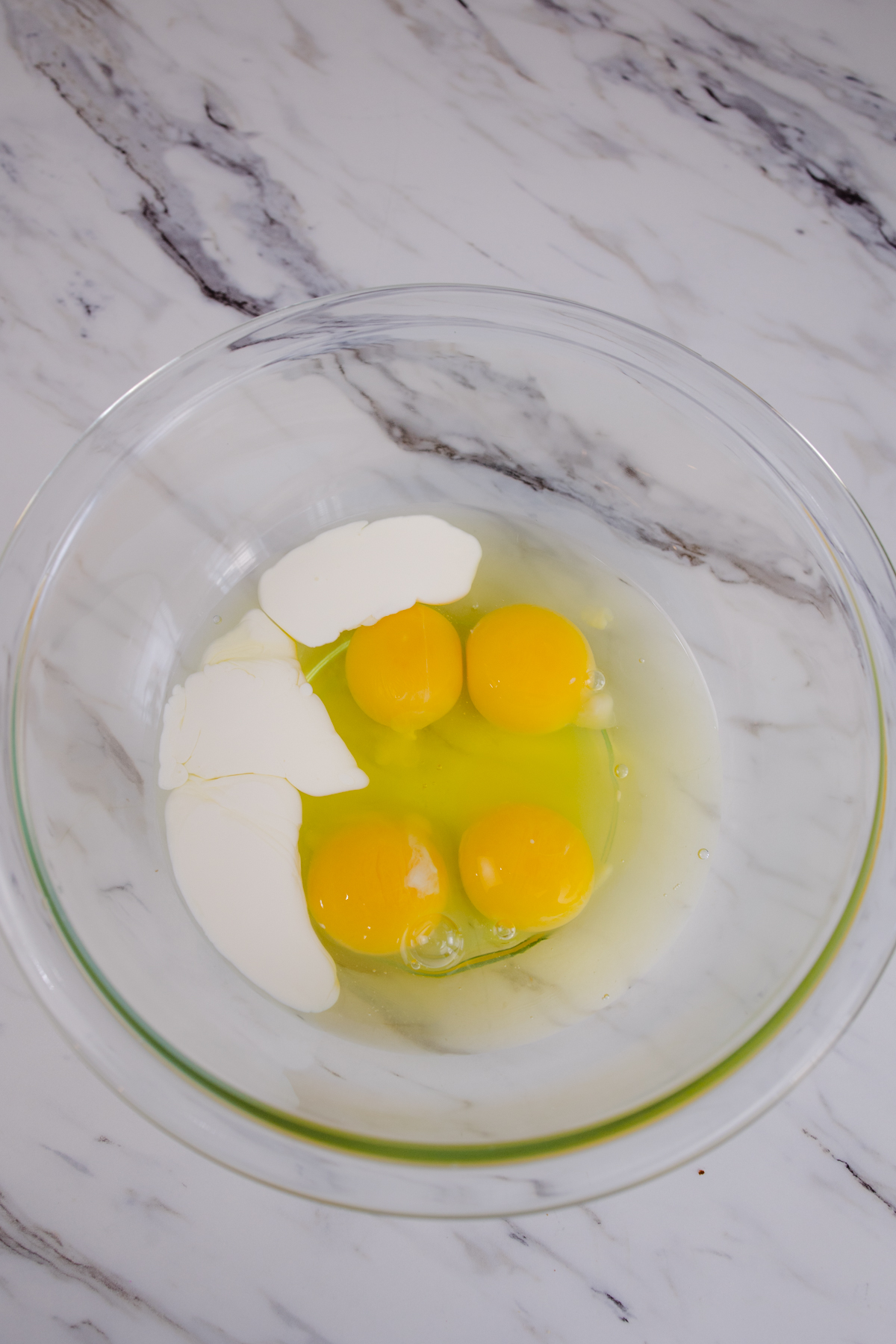 A top view of 4 egg yolks and whites in a glass mixing bowl with some milk.