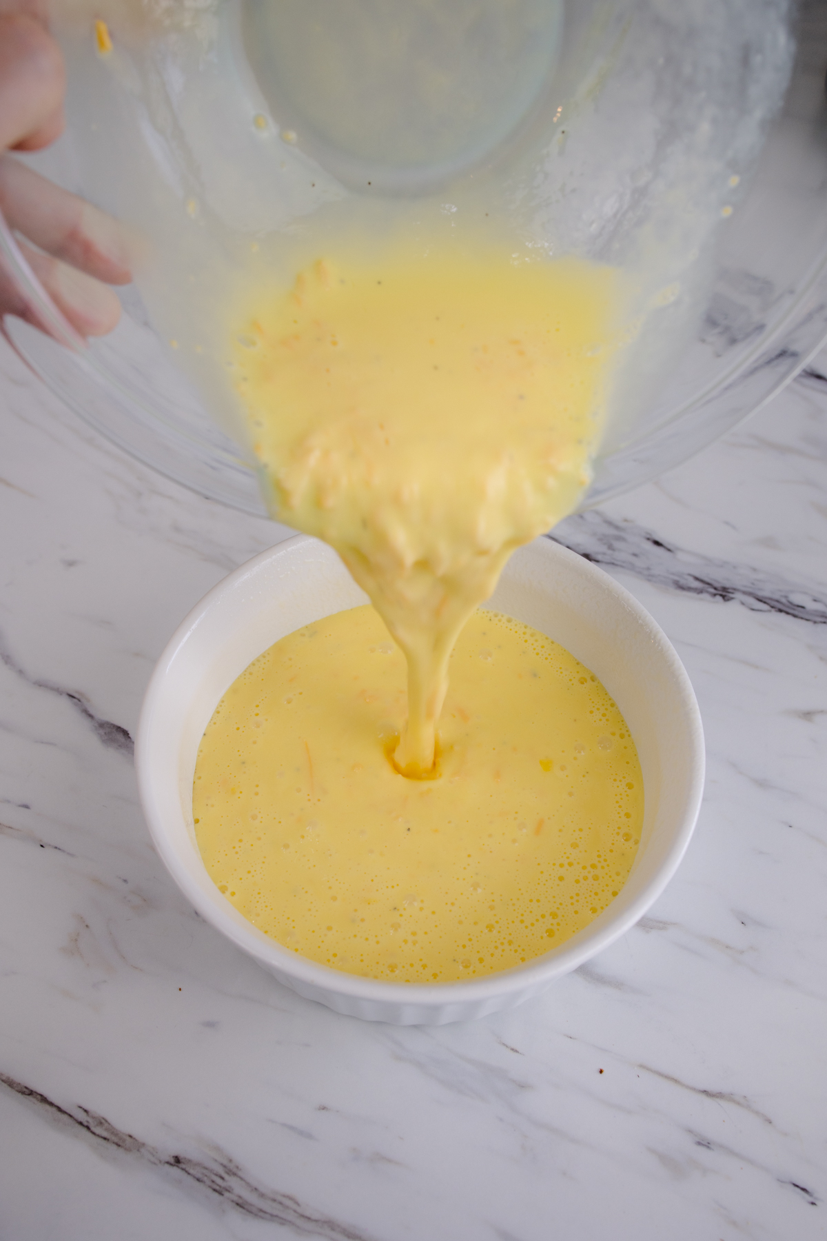 Close up view of scrambled egg mixture being transferred from a glass mixing bowl to a white bowl.