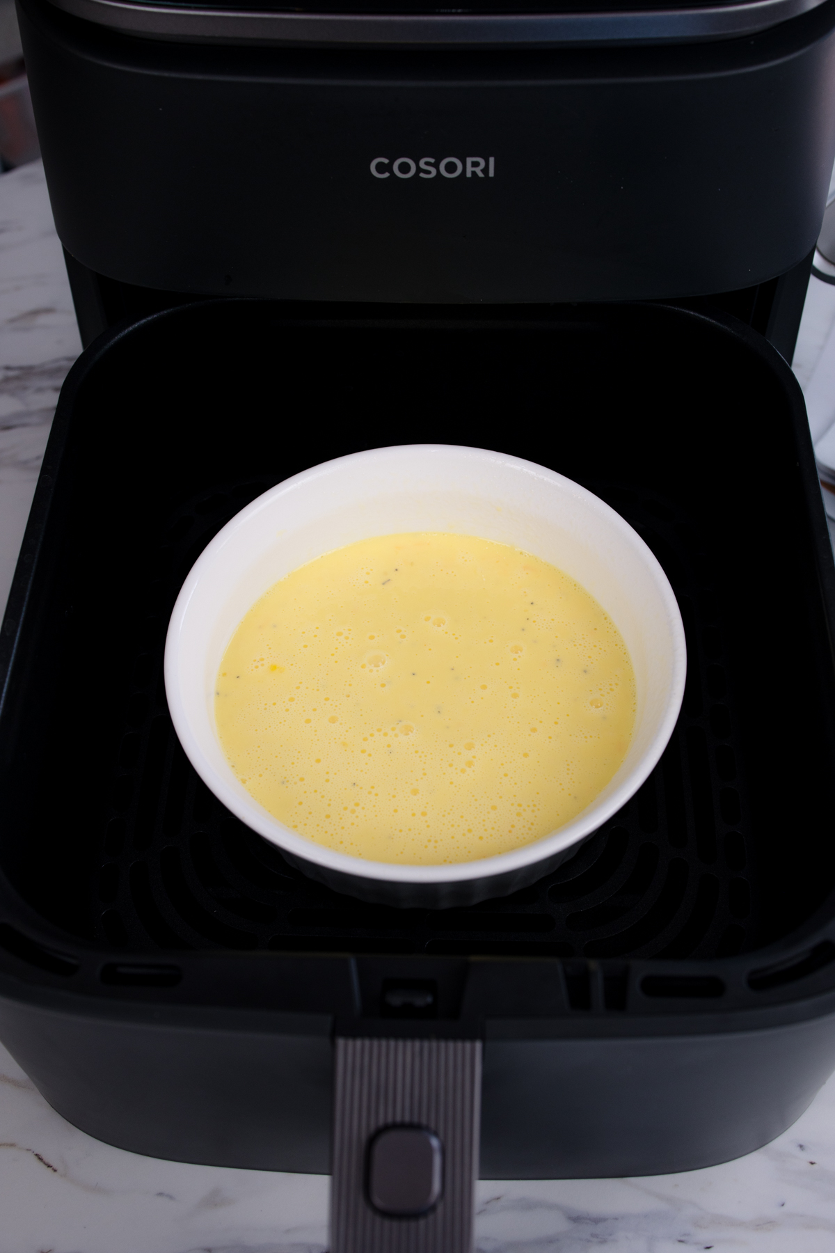 Close up view of scrambled egg mixture in a white bowl in an air fryer.