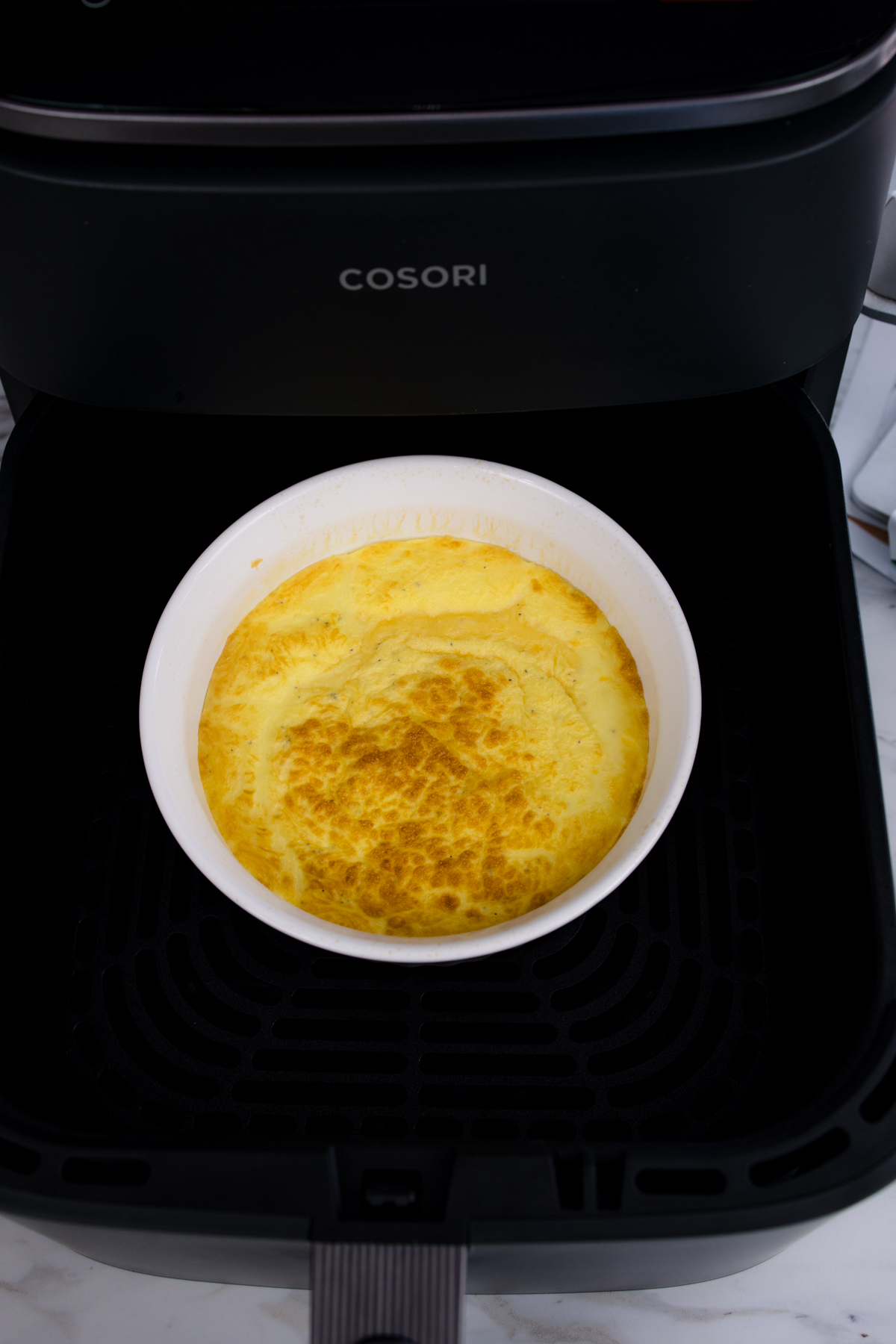 Close up view of partially-cooked scrambled egg mixture in a white bowl in an air fryer.