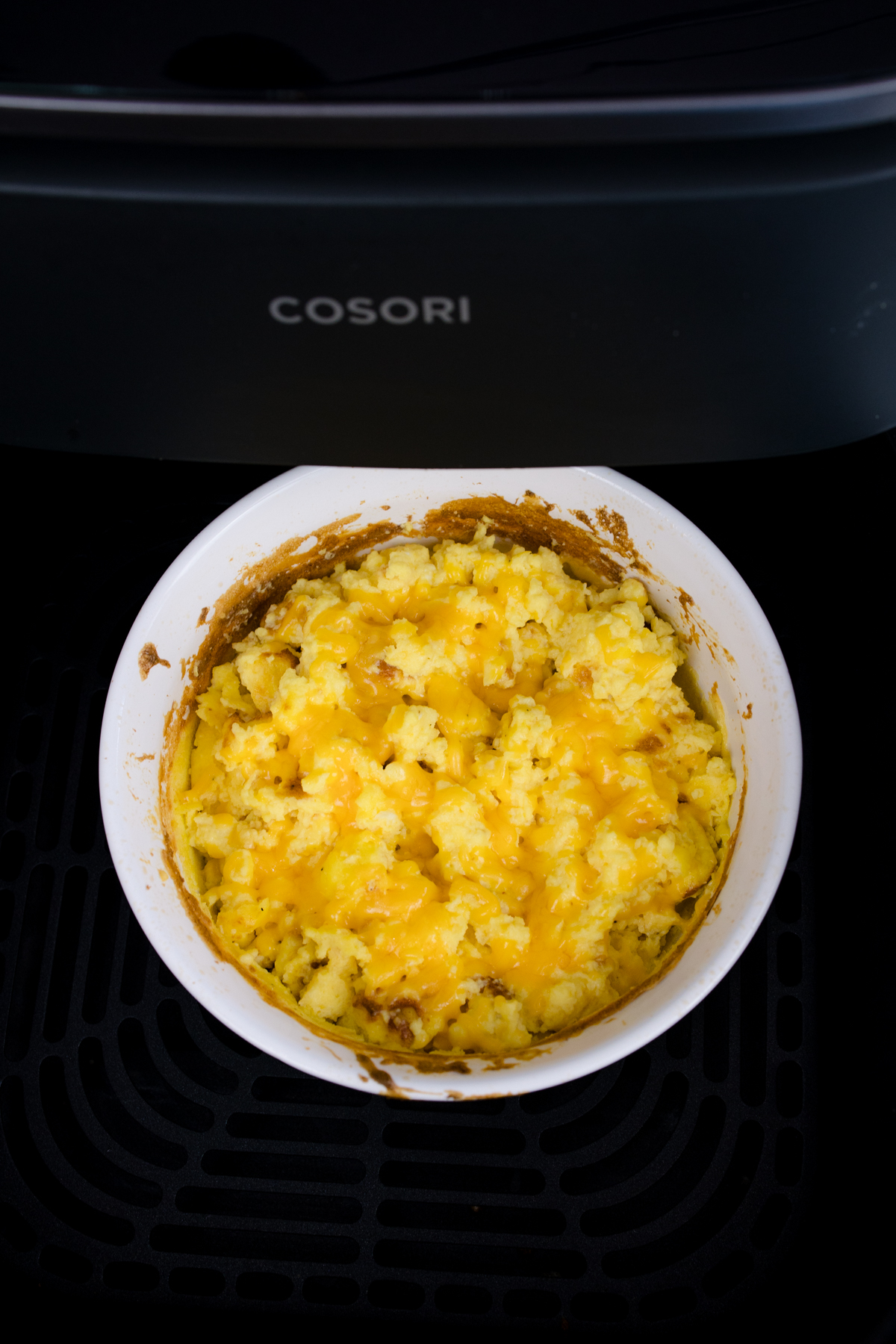 Close up view of stirred cooked scrambled egg mixture in a white bowl in an air fryer.