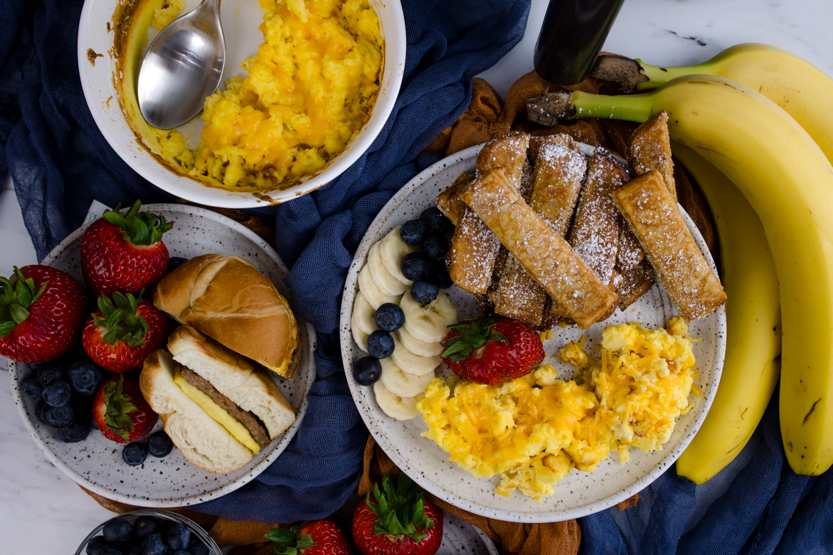 Air Fryer Scrambled Eggs on a white plate with other breakfast items, next to a bowl of scrambled eggs, and another plate with food on it.