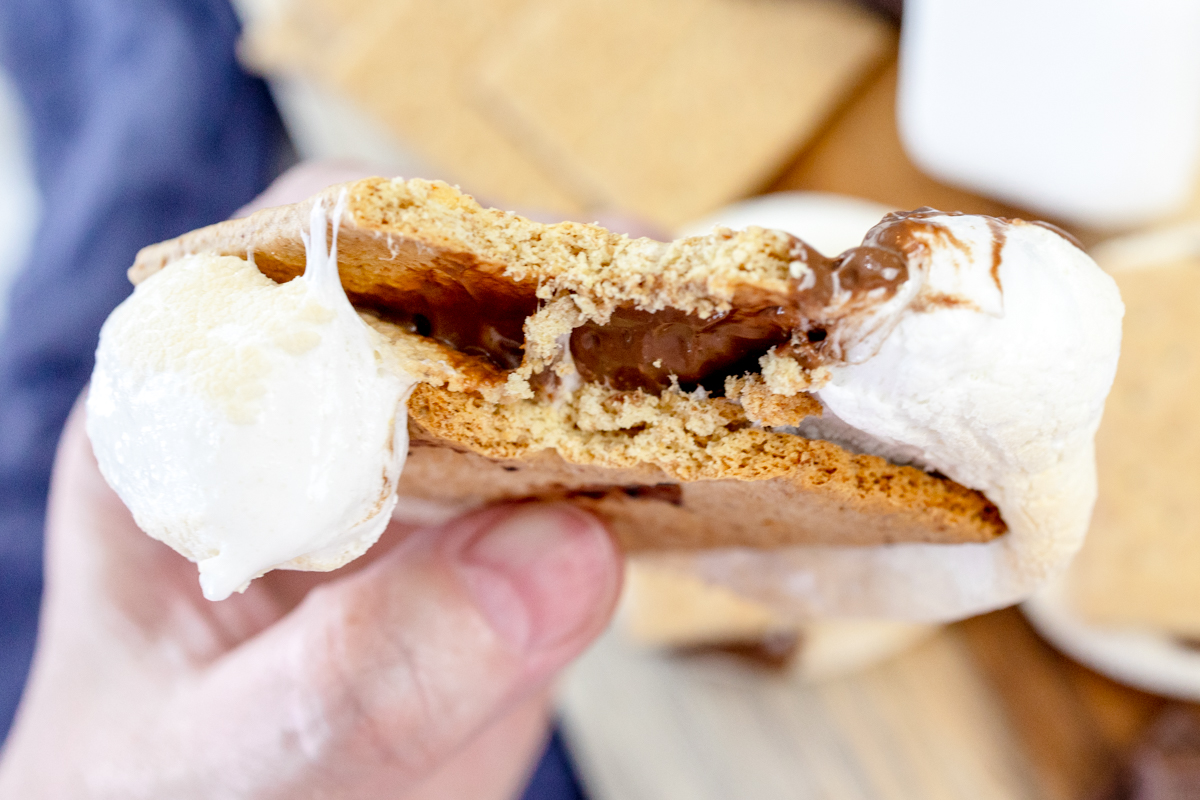 A hand squeezing an Air Fryer Smore so that the melted chocolate and gooey marshmallow spills out of the sides.