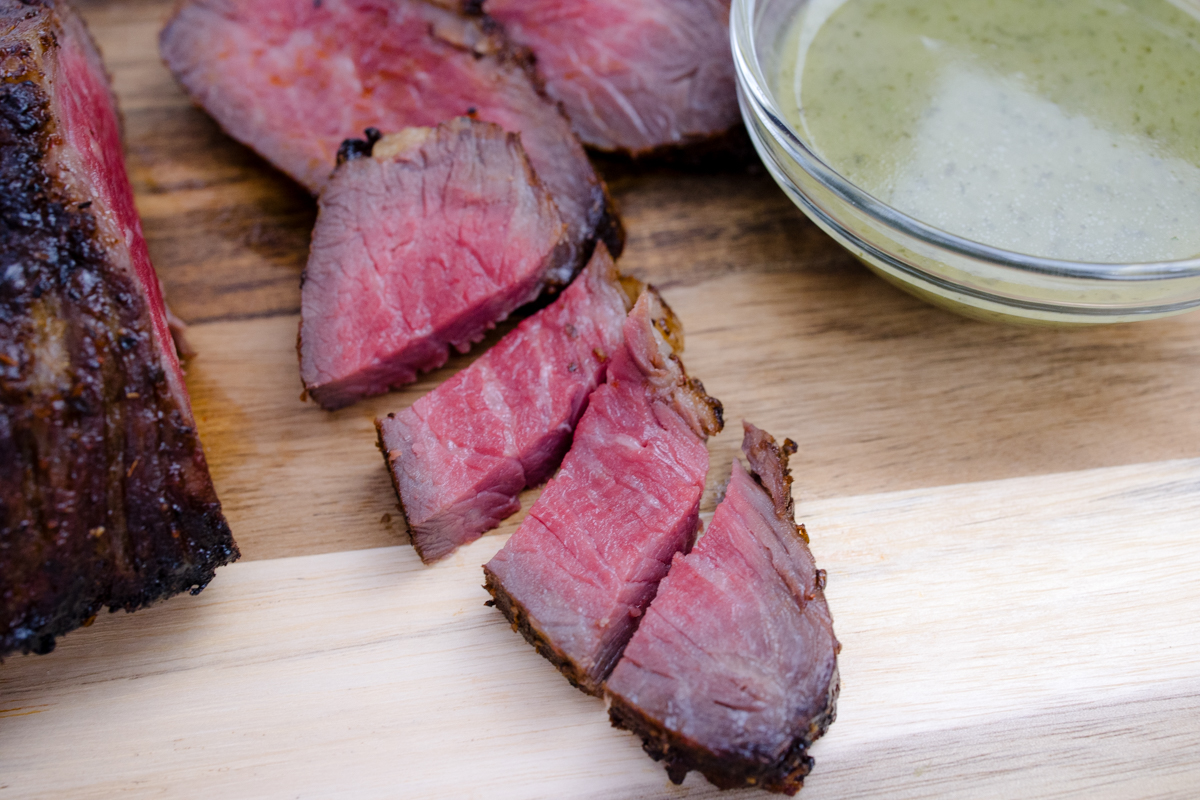 Medium rare Air Fried Tri Tip, in slices on a wooden surface, next to a bowl of sauce.