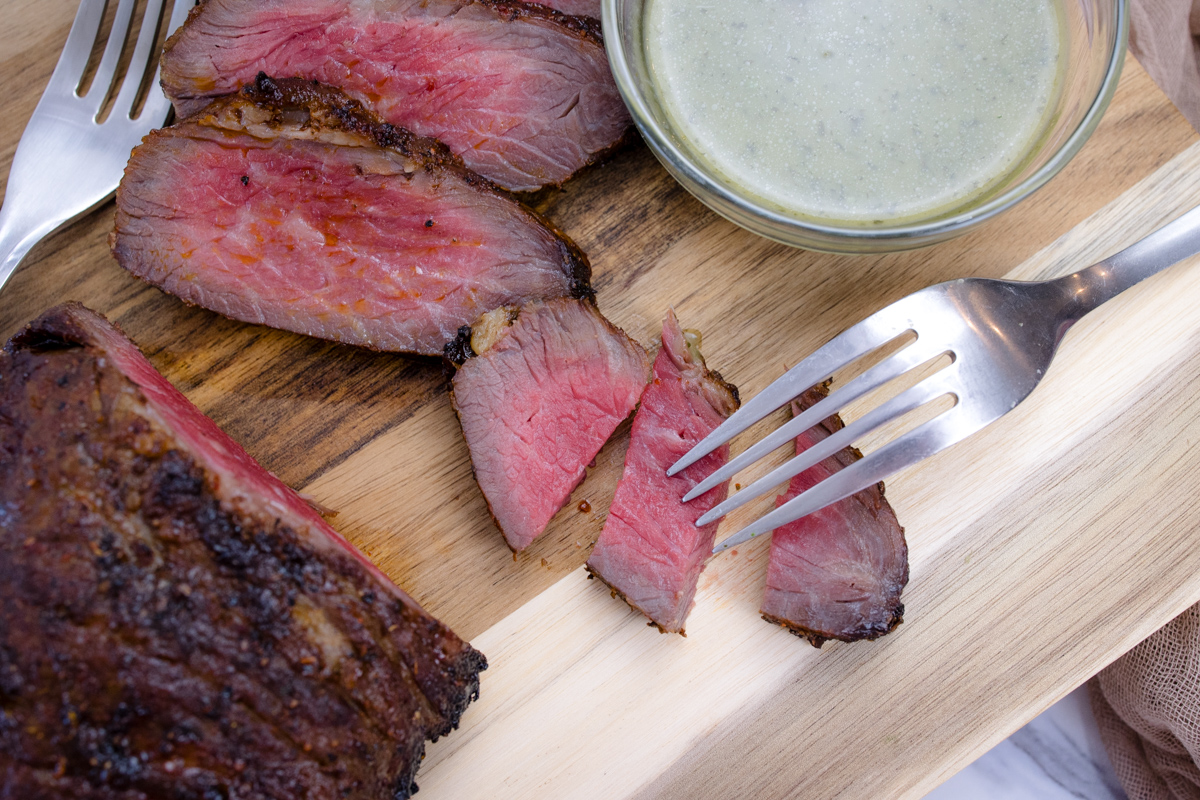 Medium rare Air Fried Tri Tip, in slices on a wooden surface, next to a bowl of sauce.