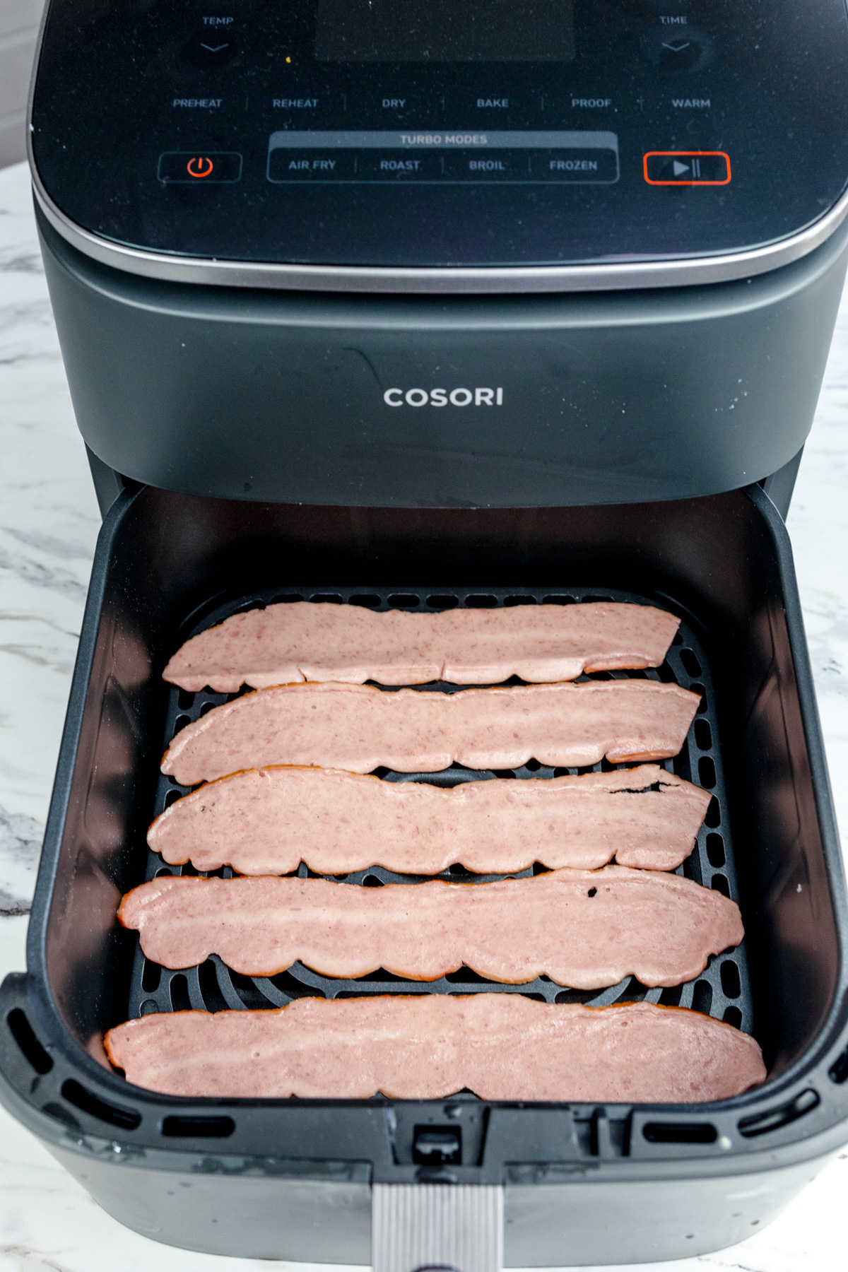 Uncooked turkey bacon in an air fryer basket.