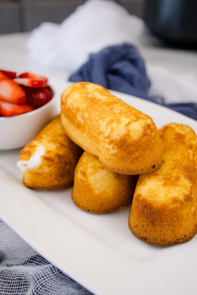 Air Fryer Twinkies on a white serving plate that has a bowl of berries on it.