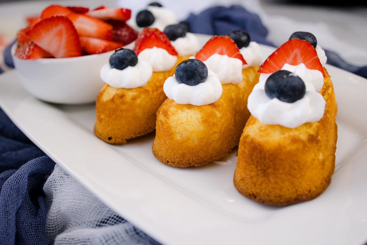 Air Fryer Twinkies topped with whipped cream and berries, on a white serving plate that has a bowl of berries on it.