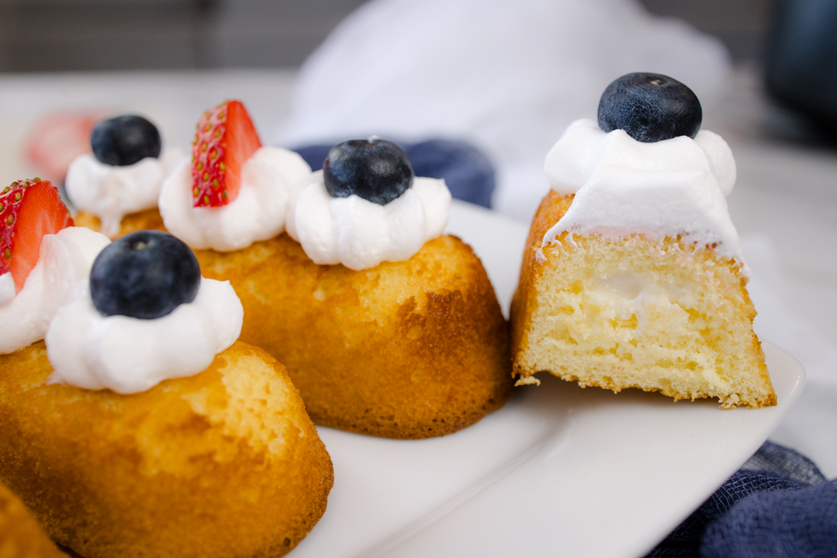 Air Fryer Twinkies topped with whipped cream and berries, on a white serving plate. One has been cut in half to reveal the inside of the Twinkie.