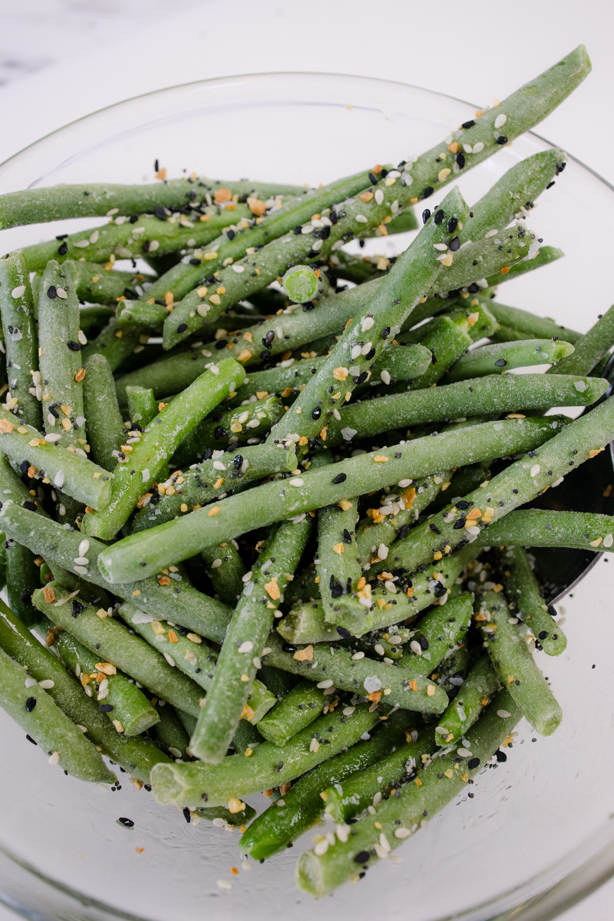 Frozen green beans being seasoned in a glass dish.