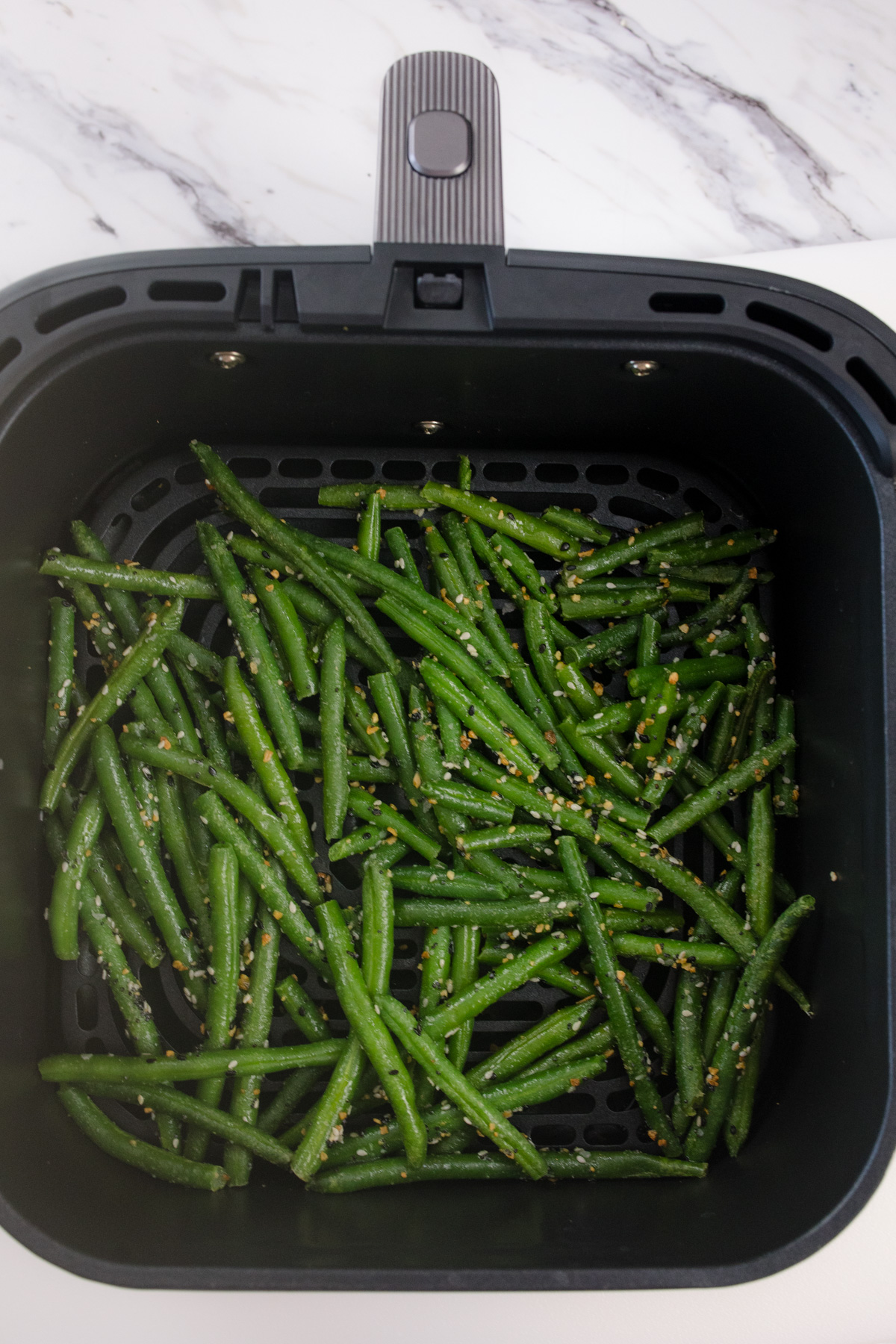 An air fryer basket with air fried green beans in it.