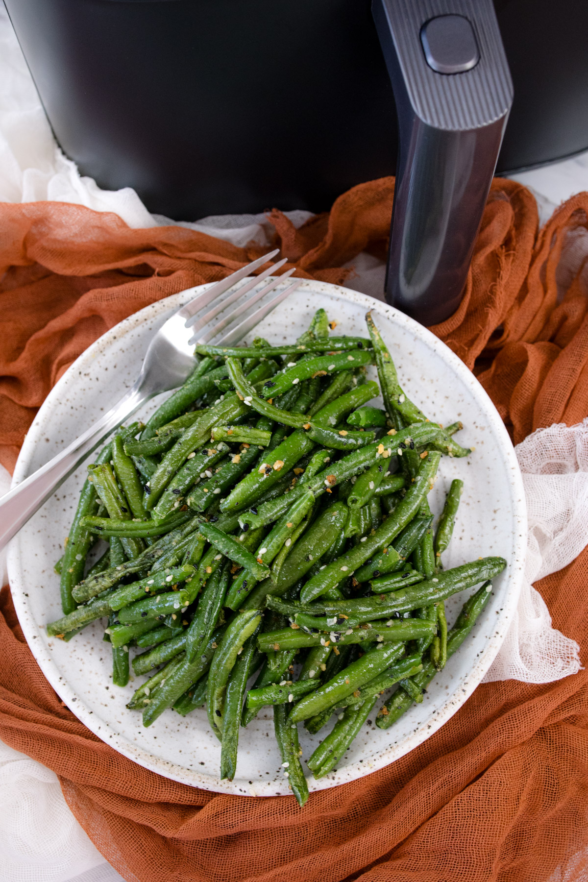 A white plate full of air fried green beans in front of an air fryer.