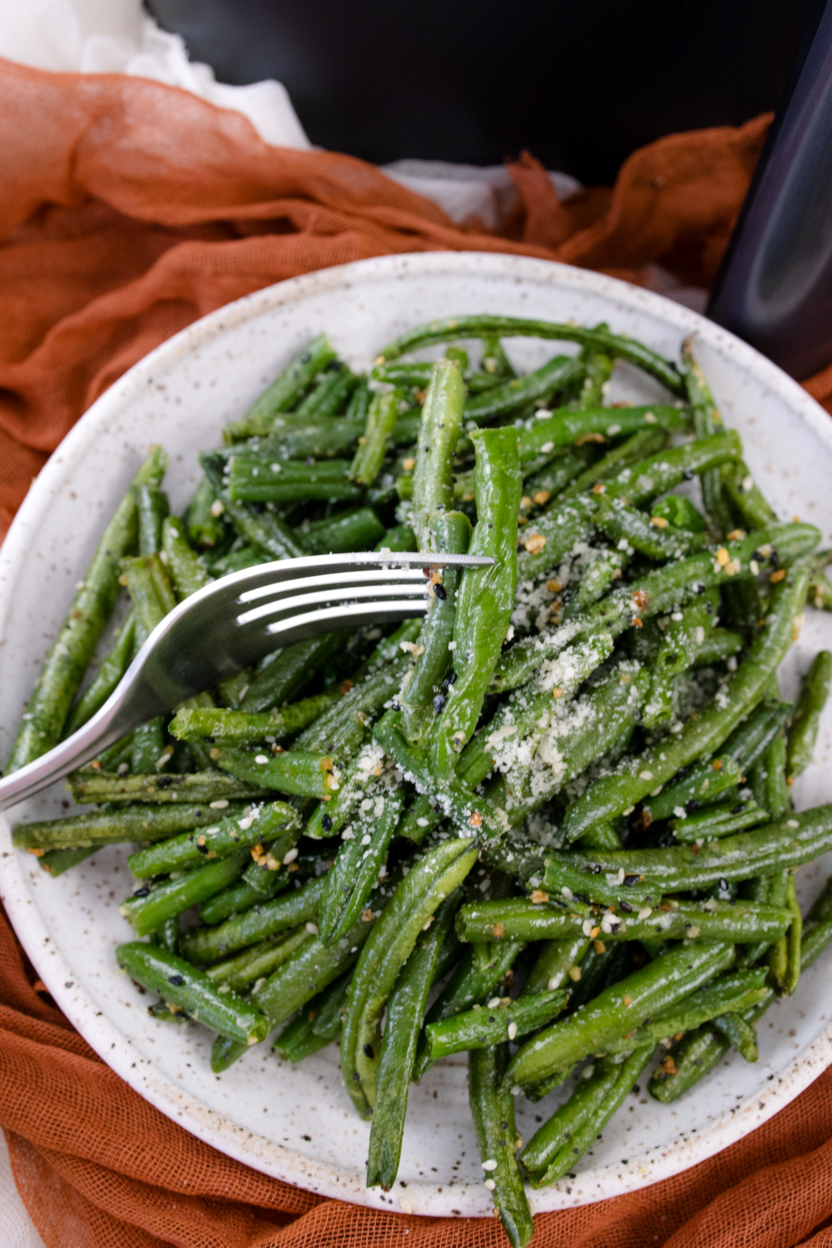 A white plate full of air fried green beans in front of an air fryer.