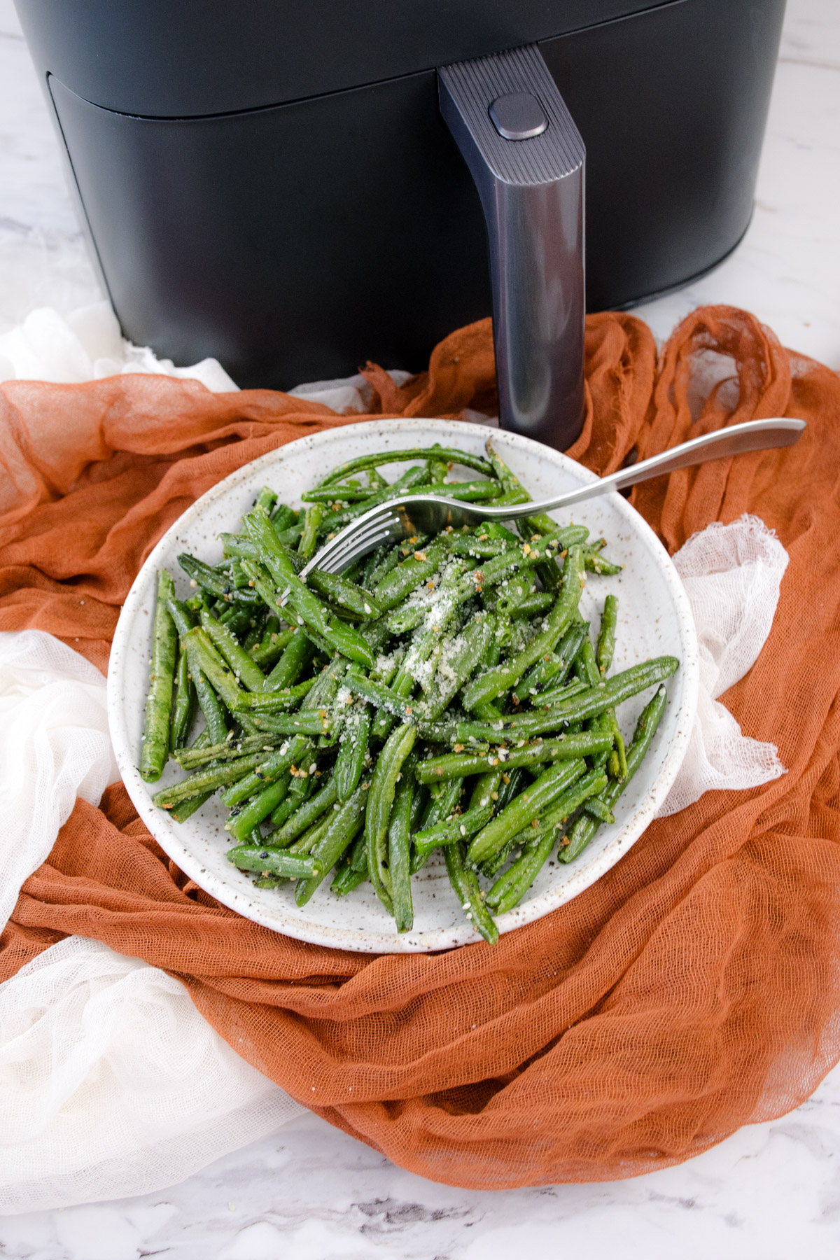 A white plate full of air fried green beans in front of an air fryer.