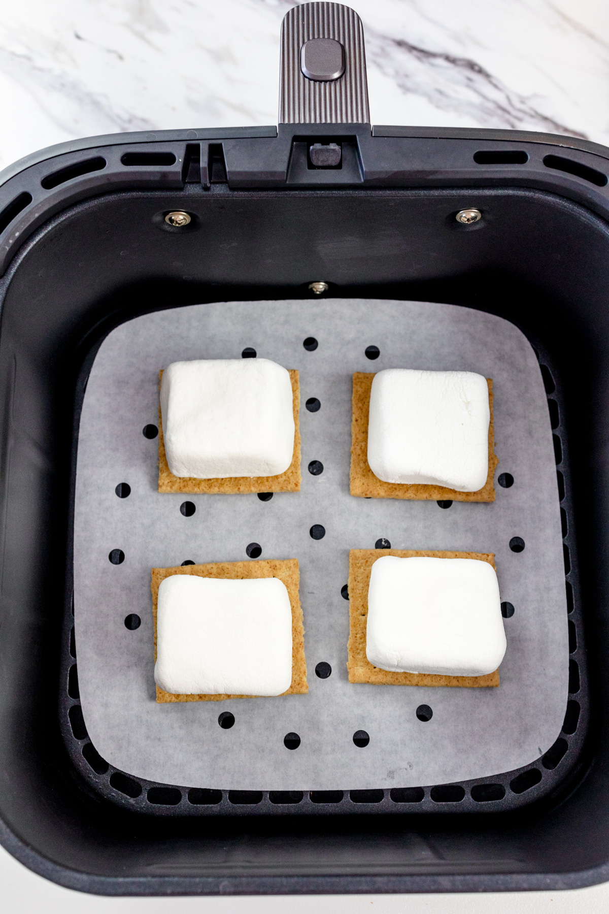 Four pre-cooked smores in an air fryer basket lined with parchment paper.