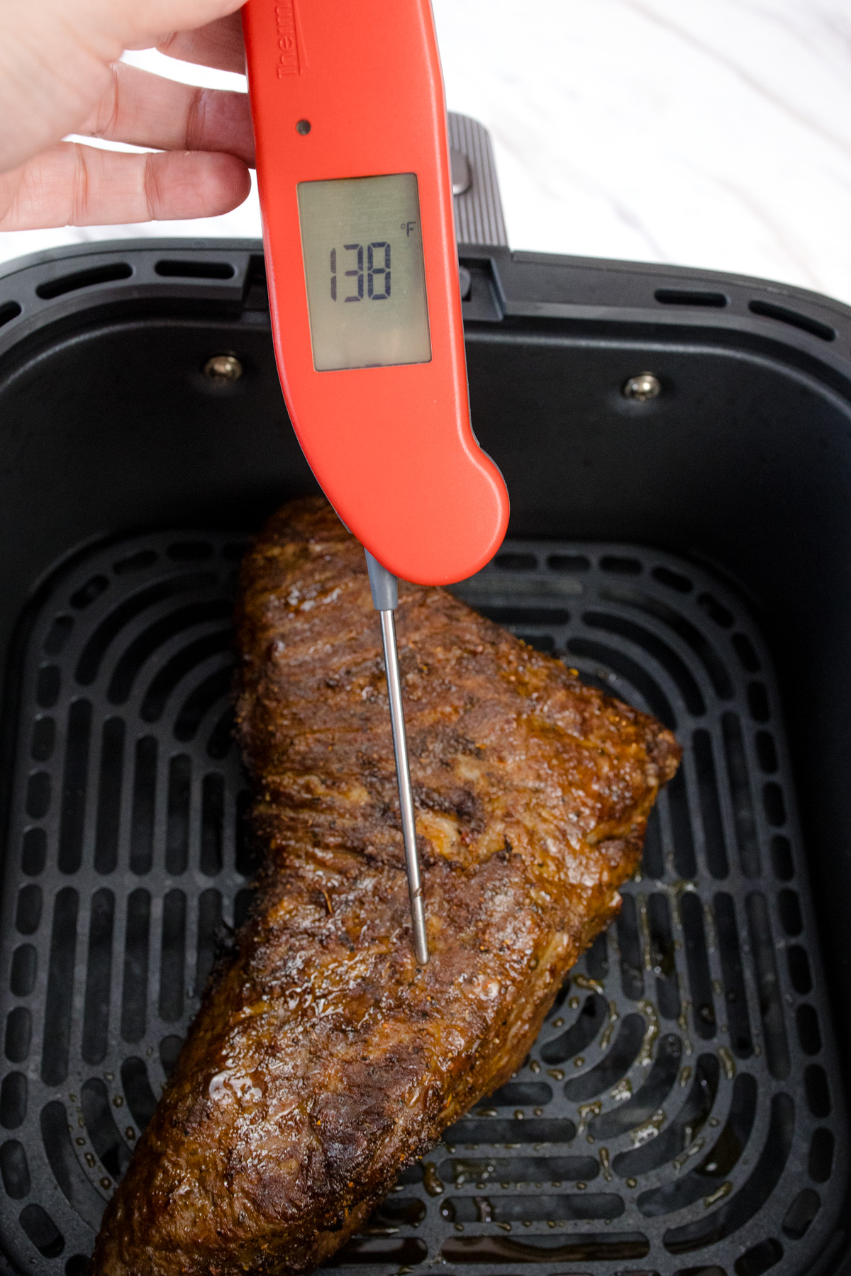 A meat thermometer being inserted into an air fried tri tip roast in an air fryer basket.