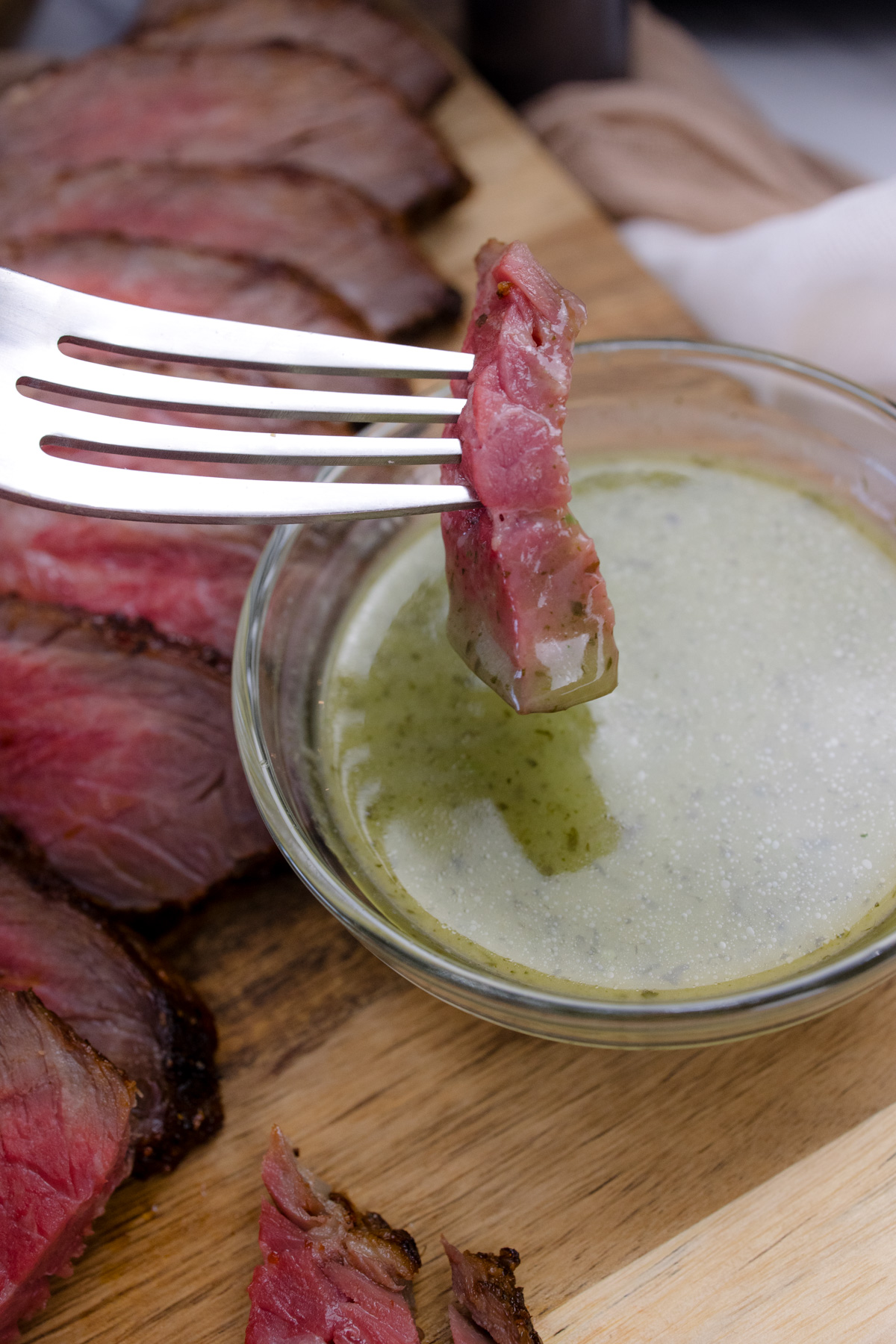 A fork dipping a slice of air fried tri tip into a bowl of sauce.