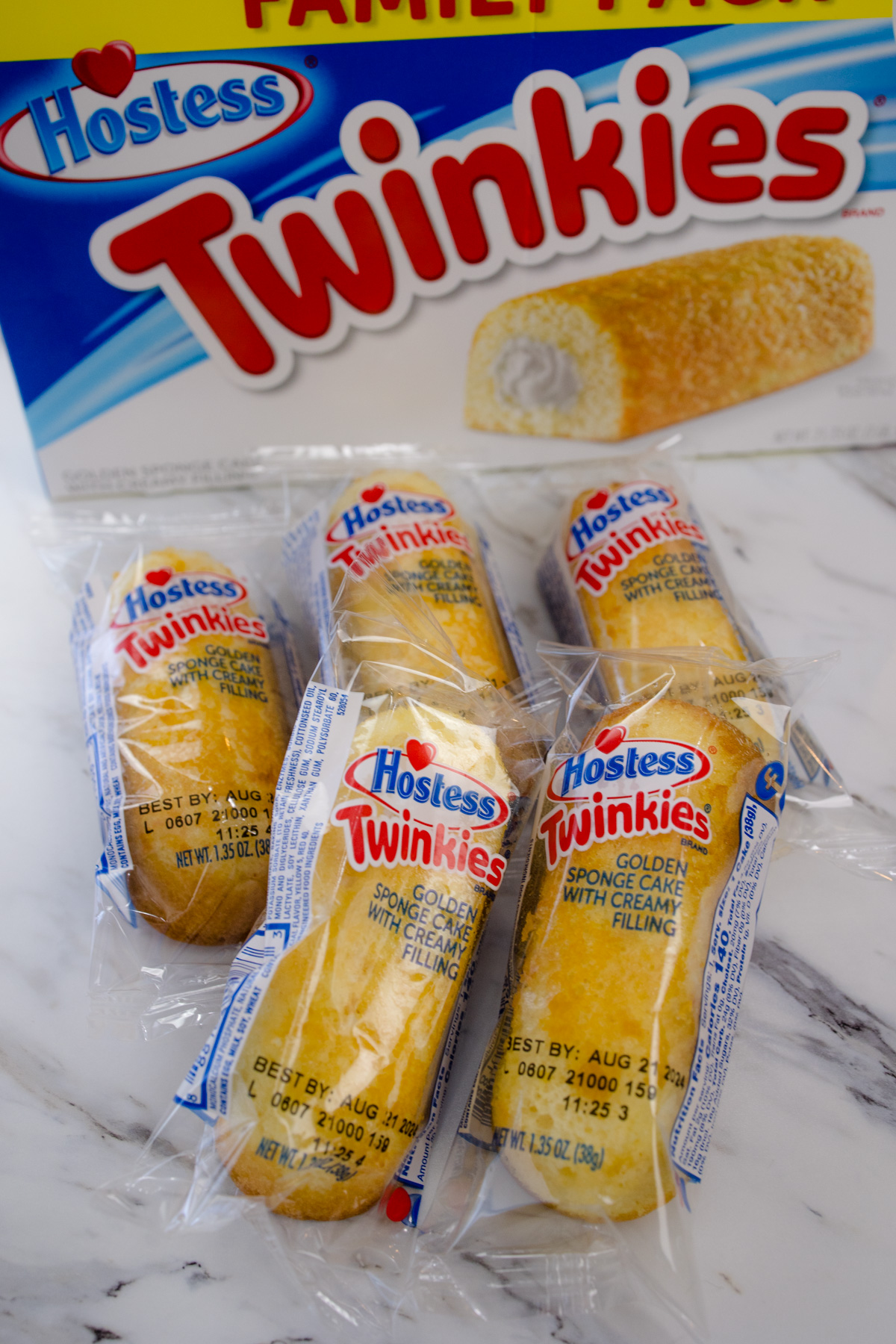 A box of Twinkies on a countertop with five Twinkies in front of it, still in their packaging.