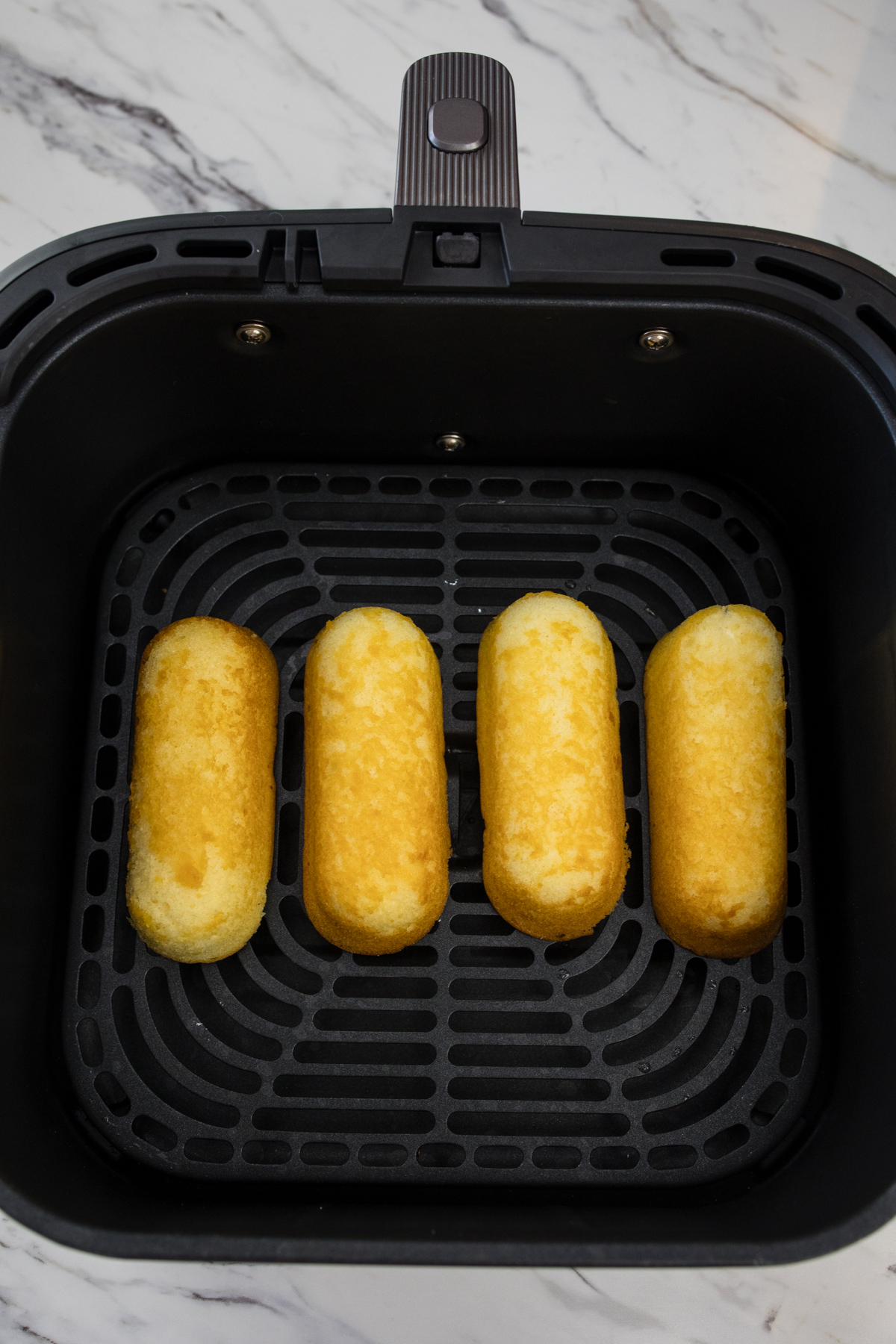 Four Twinkies in an air fryer basket.