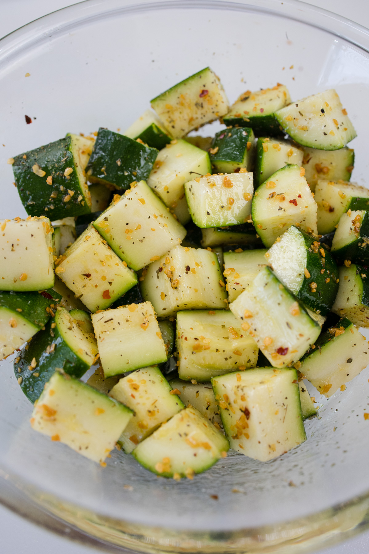 Zucchini in a bowl being seasoned.