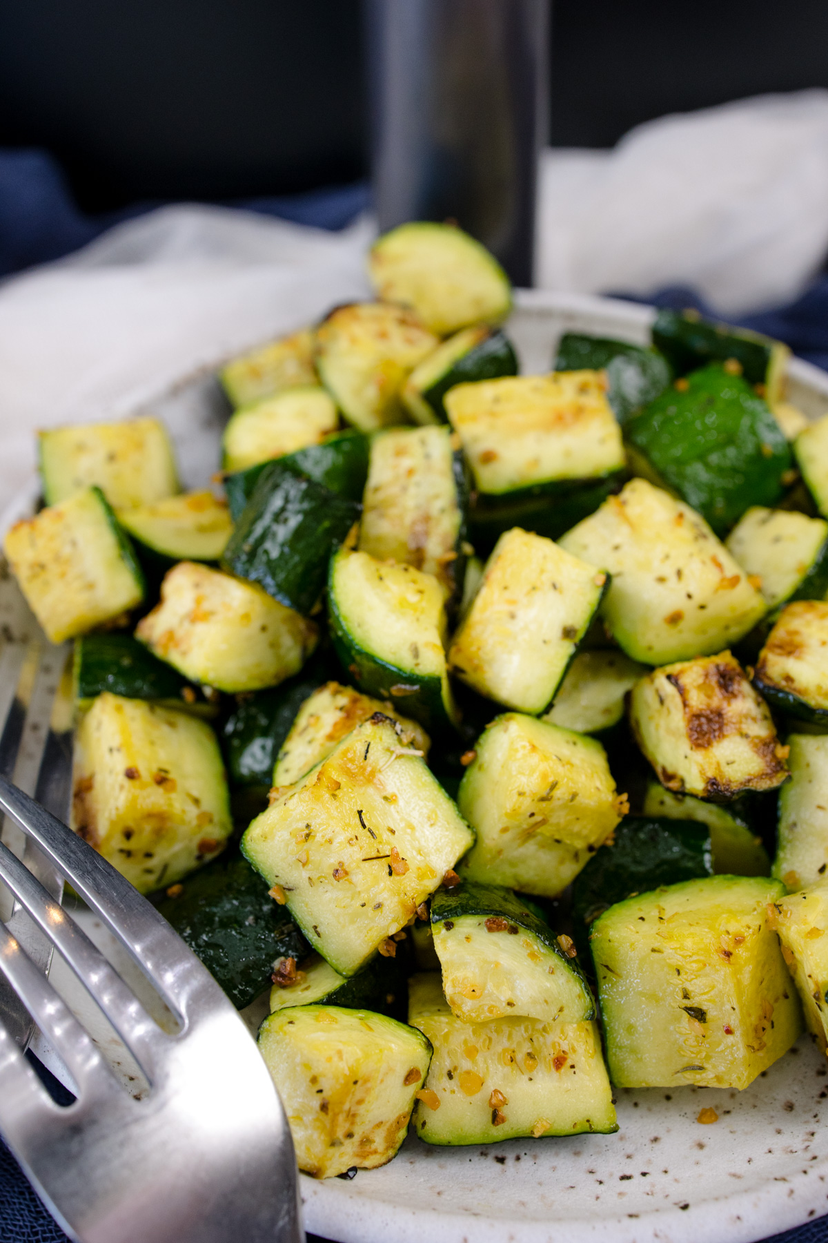 Air Fryer Zucchini on a white plate with a silver fork in the foreground and an air fryer in the background.