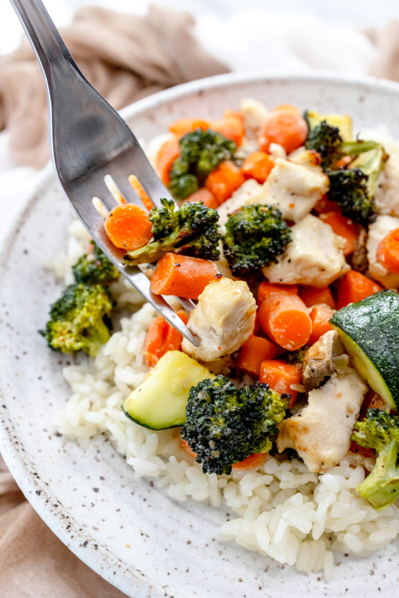 Air Fryer Chicken and Vegetables on a white plate with a silver fork scooping into the food.