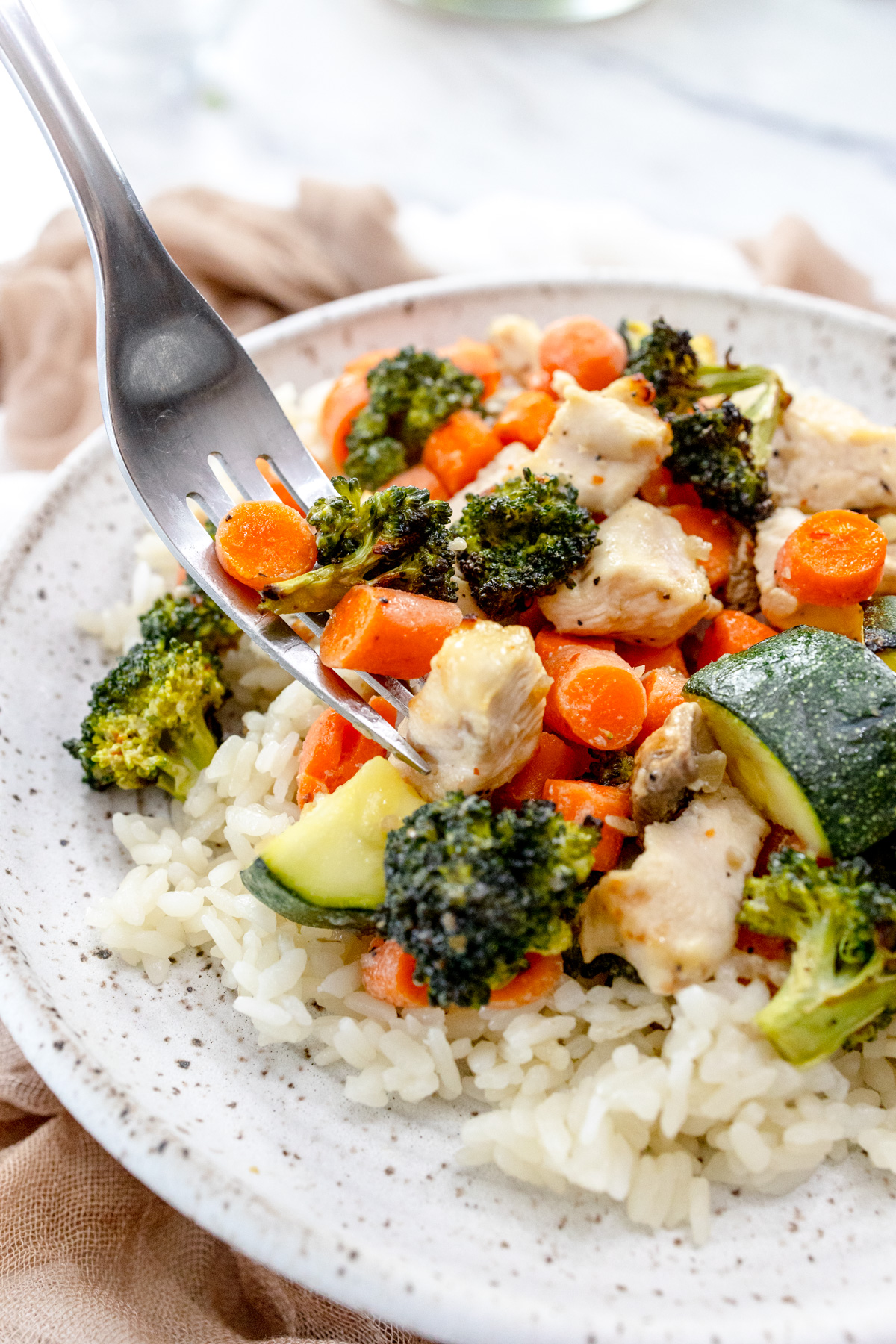 Air Fryer Chicken and Vegetables on a white plate with a silver fork scooping a forkful up.