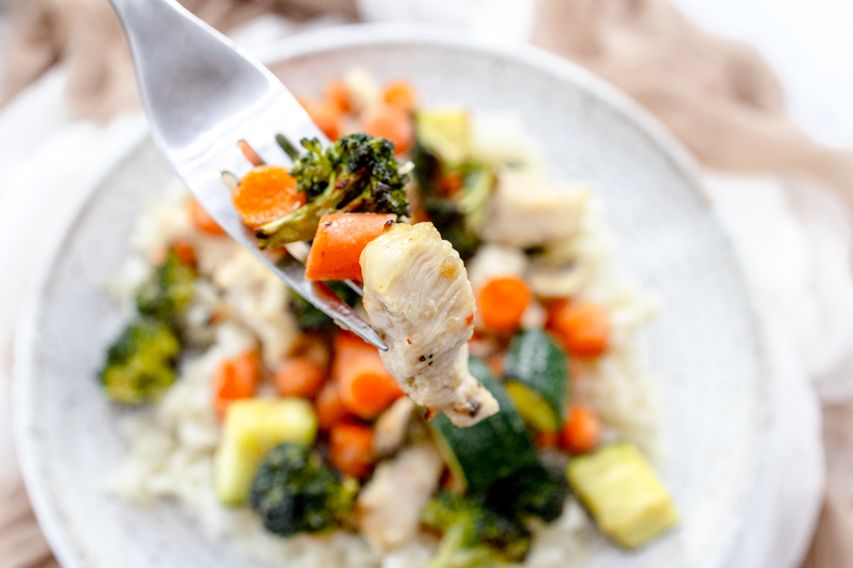 Air Fryer Chicken and Vegetables on a white plate with a silver fork scooping a forkful up.