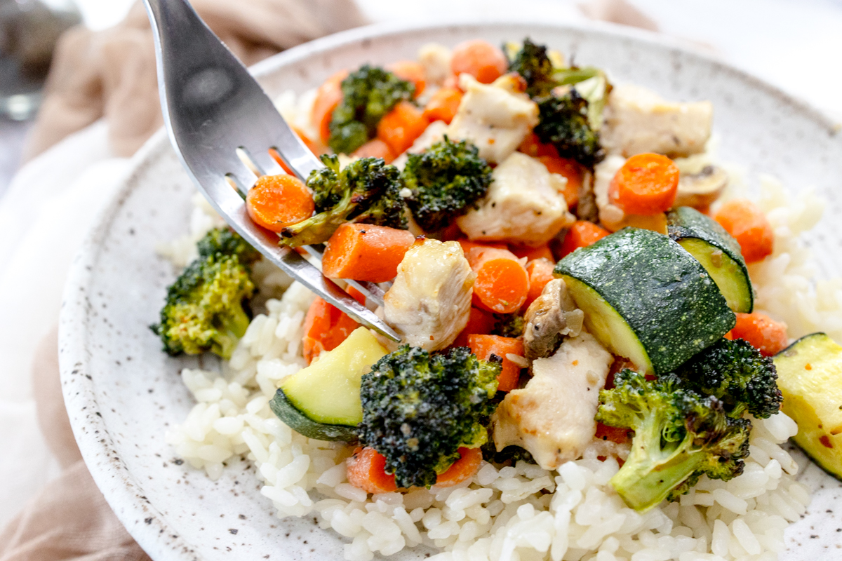 Air Fryer Chicken and Vegetables on a white plate with a silver fork scooping a forkful up.