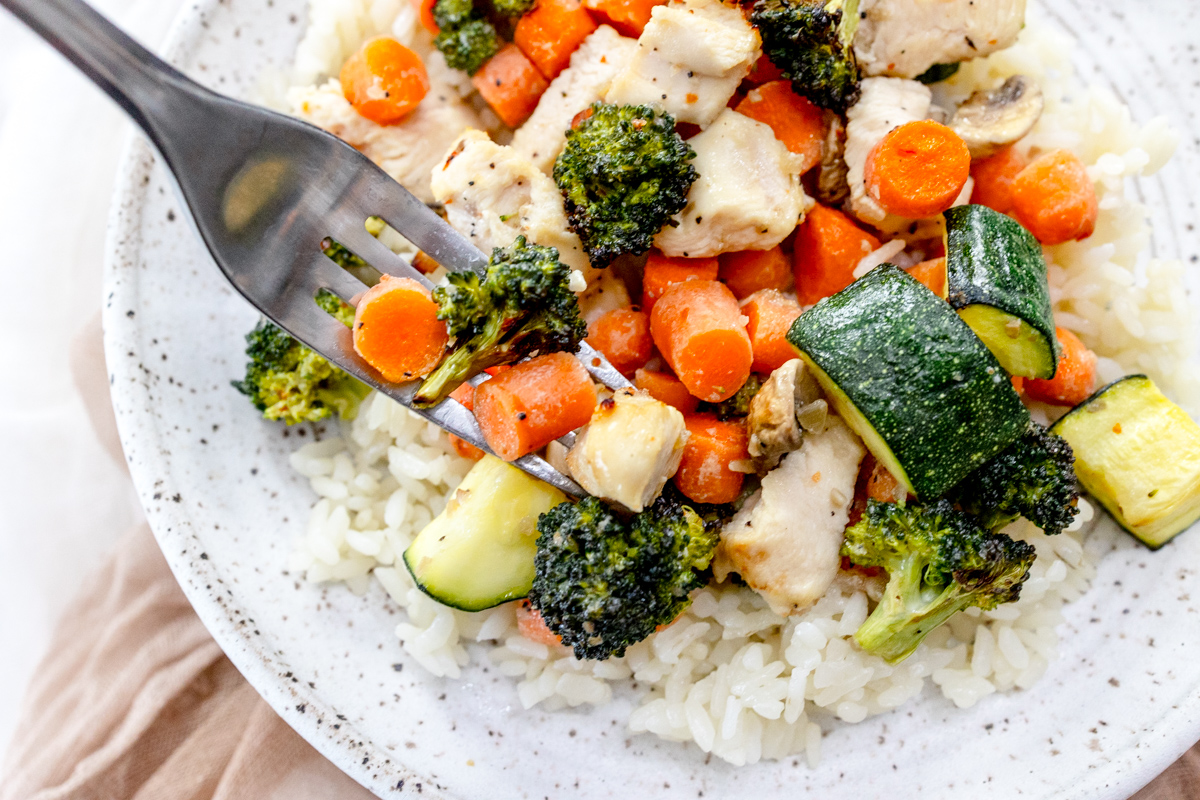 Air Fryer Chicken and Vegetables on a white plate with a silver fork scooping into the food.