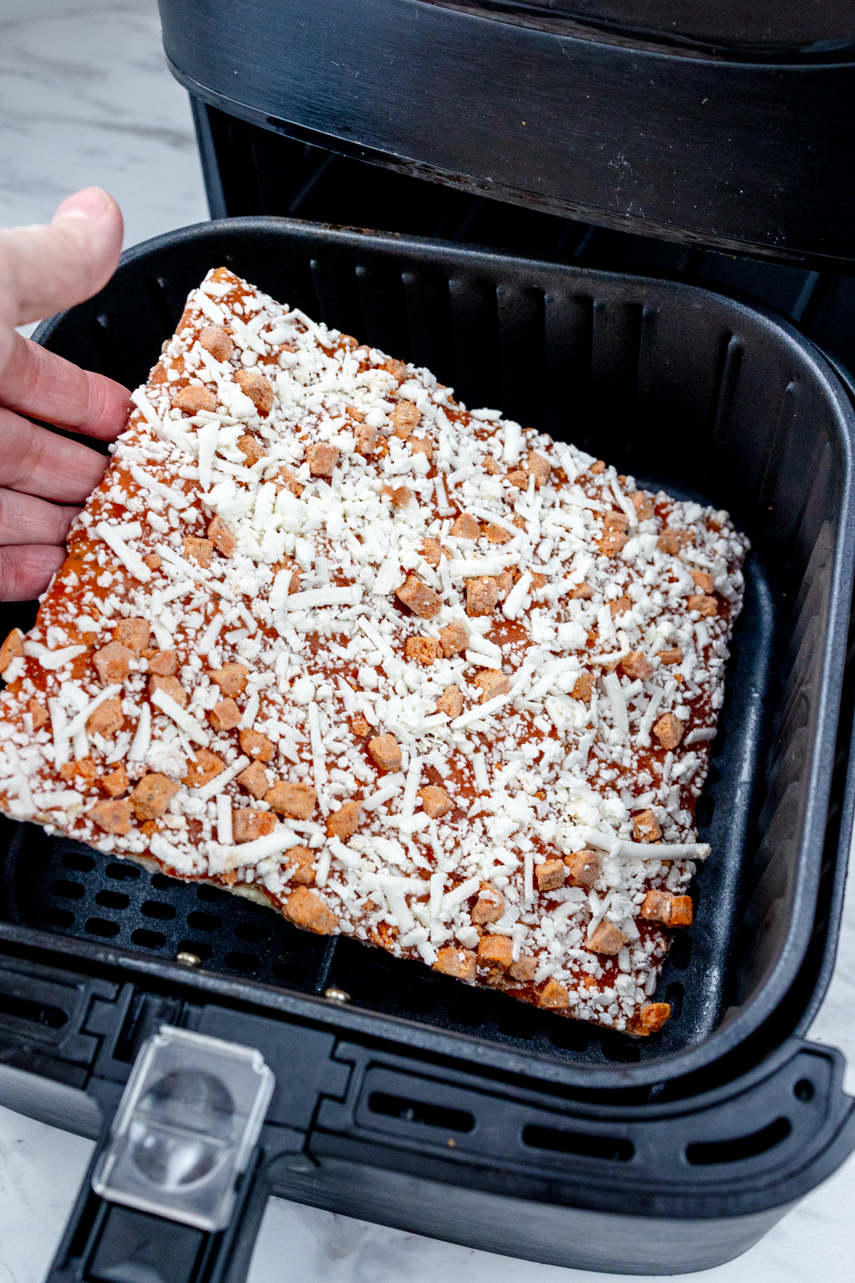 Totino's party pizza being placed in an air fryer basket.