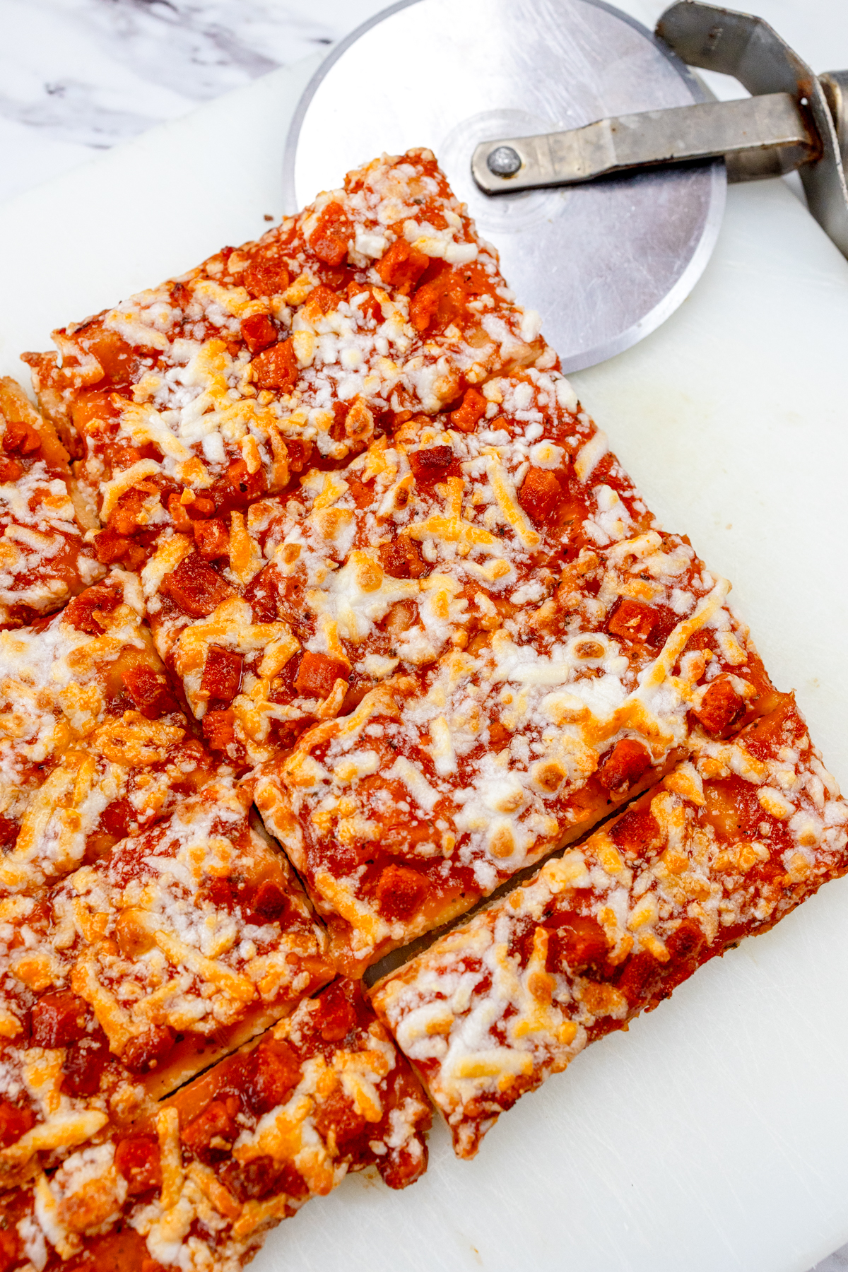 Cooked air fryer pizza on a white surface with a pizza slicer next to it.