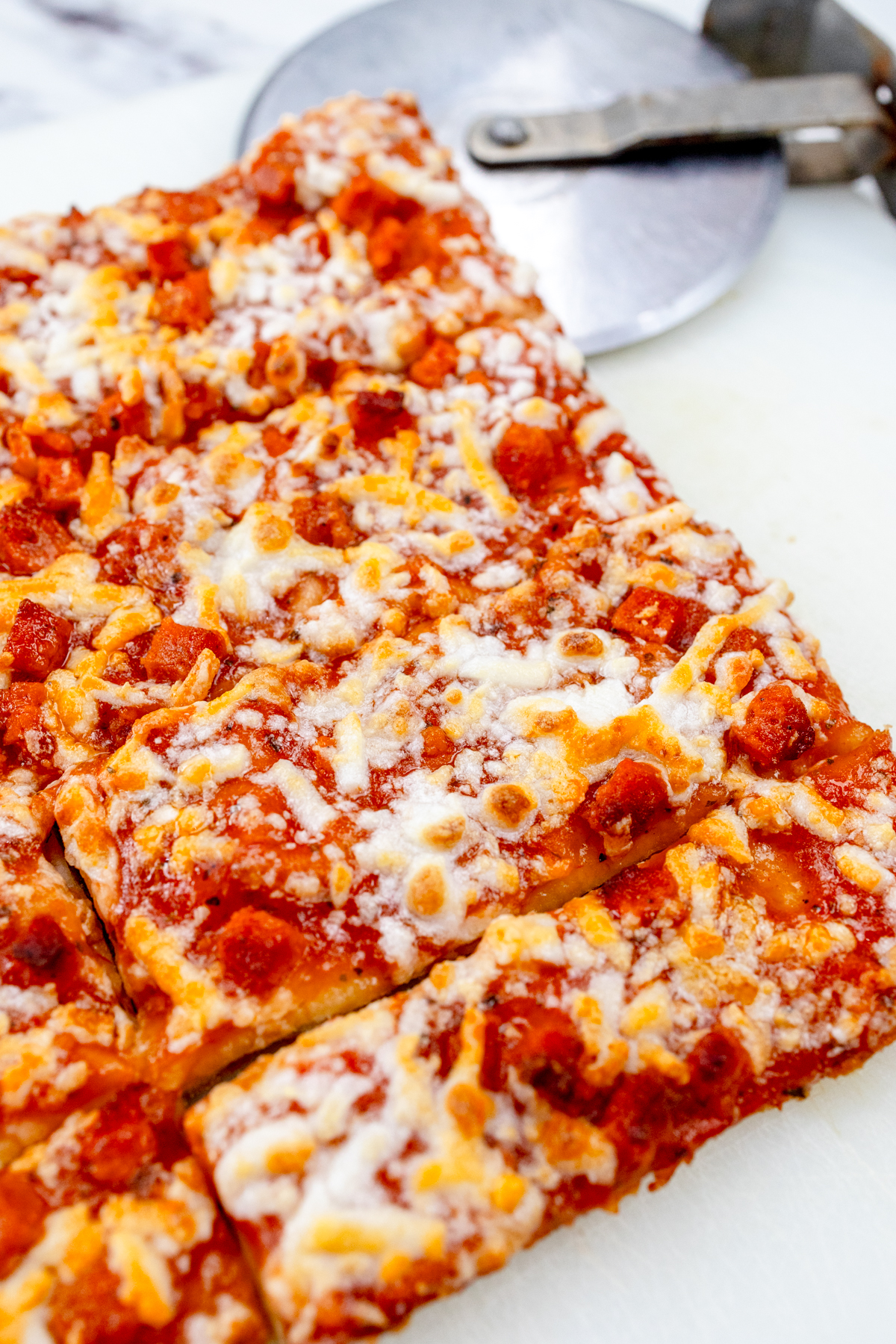 Cooked air fryer pizza on a white surface with a pizza slicer next to it.