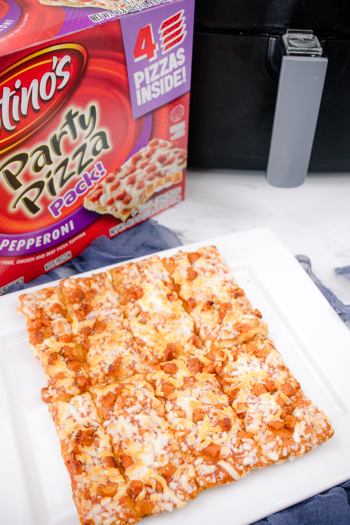 Cooked air fryer pizza on a white surface in front of the packaging and an air fryer.